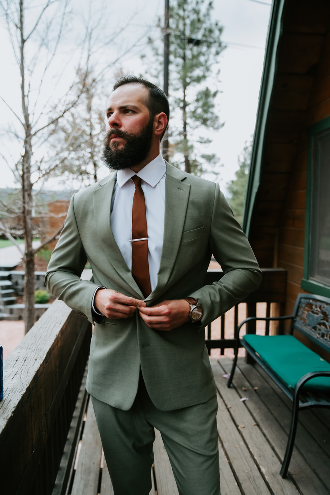 Groom buttoning his sage green suit jacket on the cabin porch before the wedding at Cabins at Strawberry Hill.