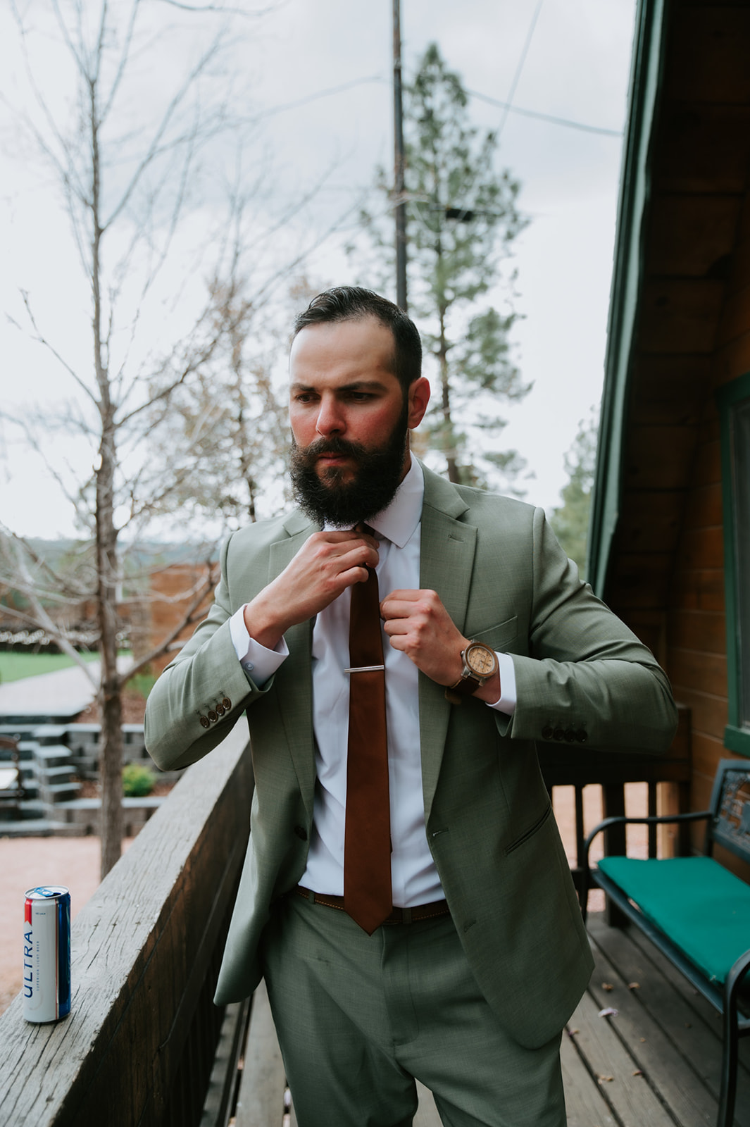 Groom adjusting his tie while getting ready on the porch of a mountain cabin in Strawberry, Arizona.