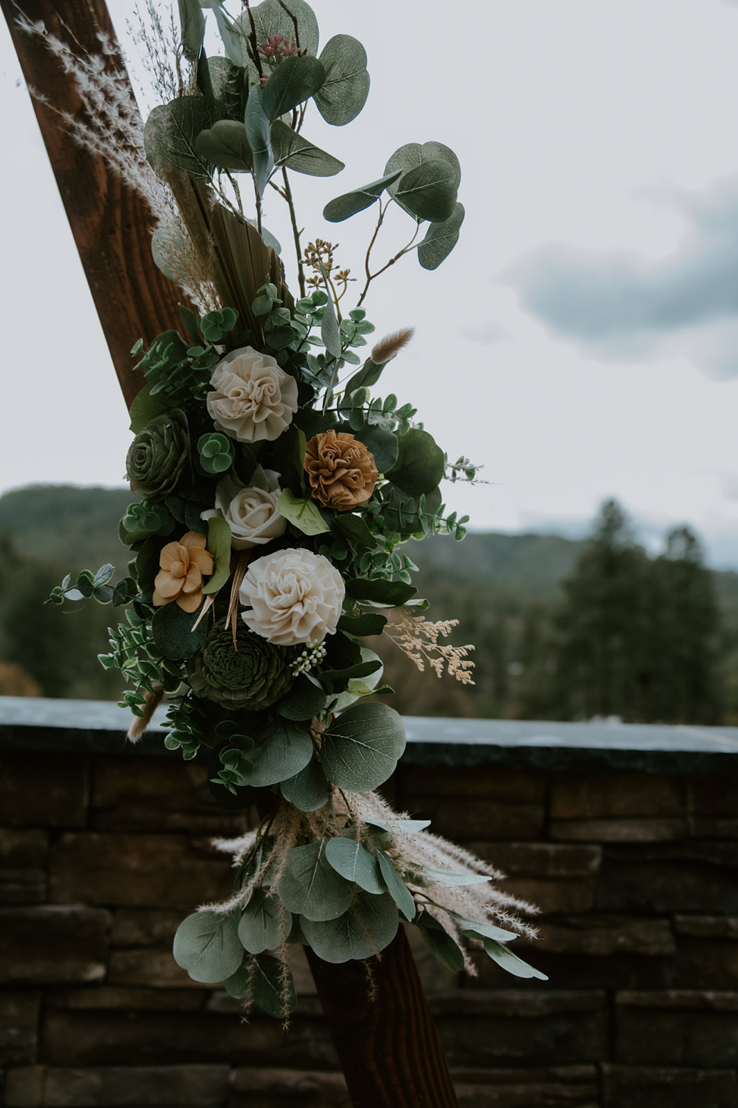 Rustic floral arrangement decorating a wooden wedding arch with mountain views in the background.
