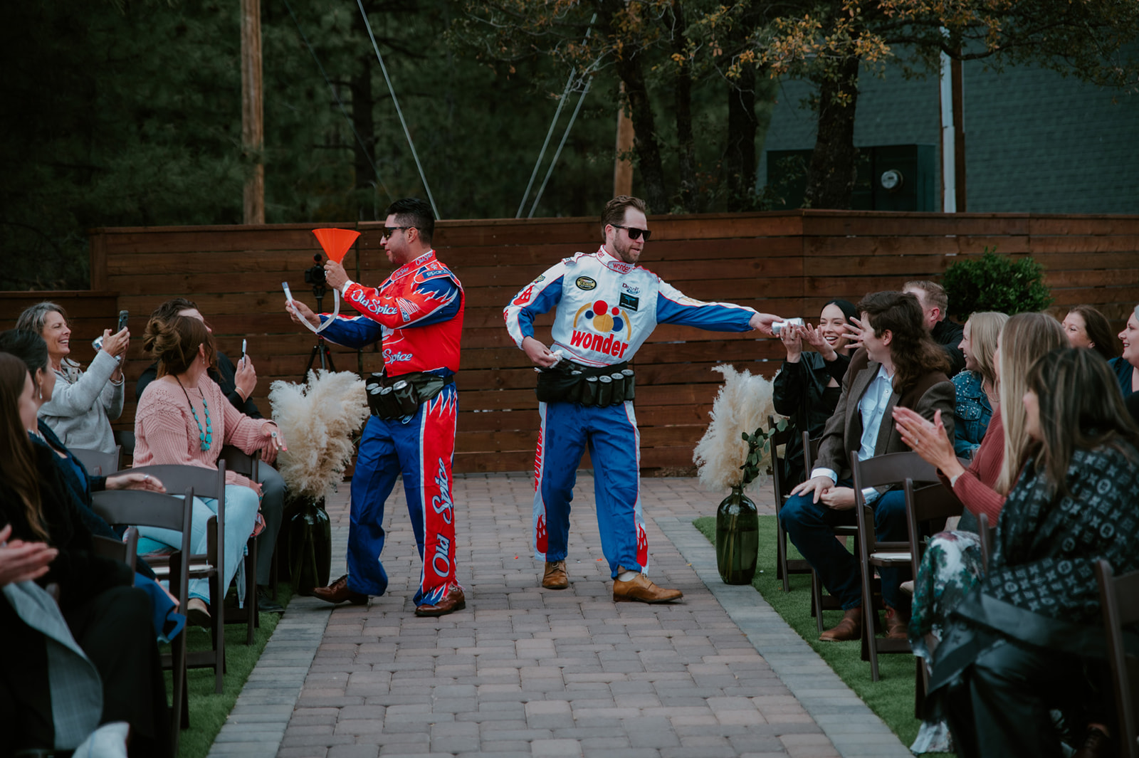 Wedding entertainers in colorful racing suits interact with guests during a lively outdoor ceremony entrance.
