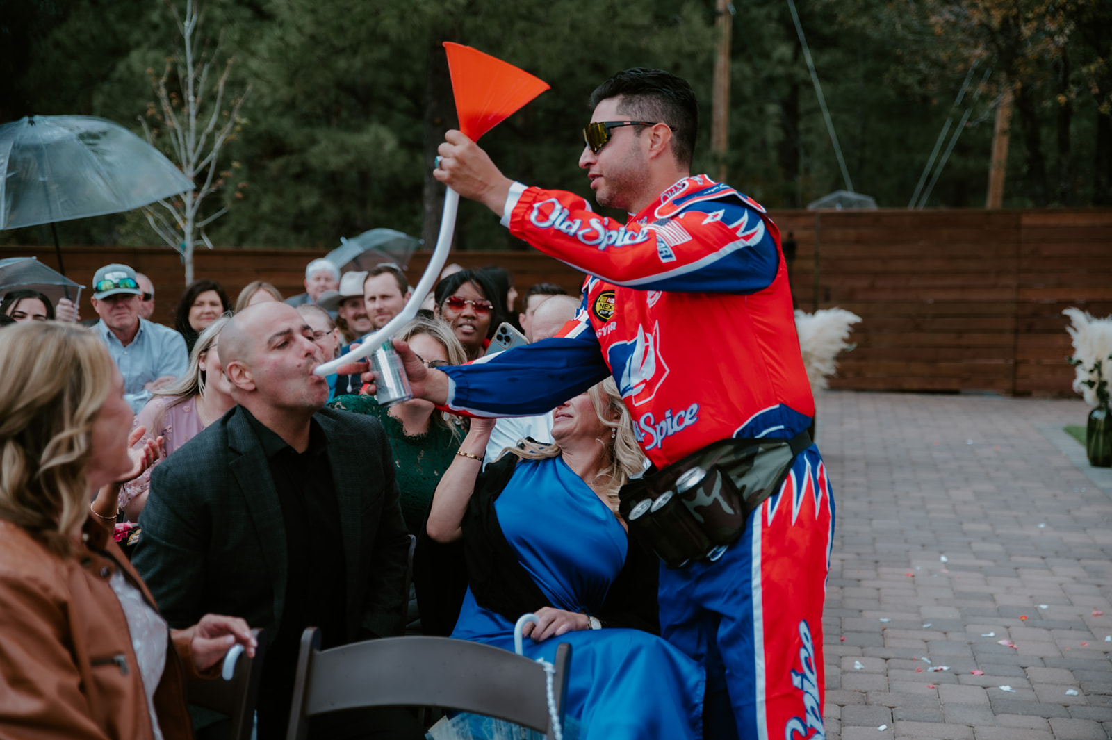 Performer in a racing suit pours a drink through a funnel for a wedding guest during the ceremony entertainment.
