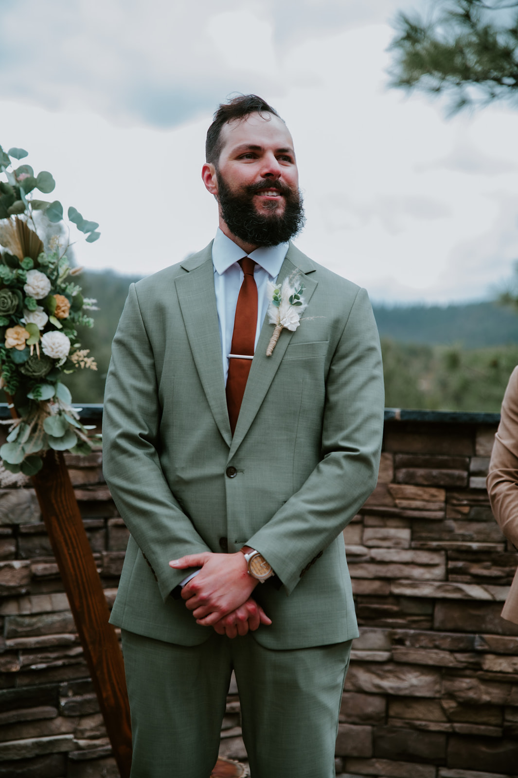 Groom in a sage green suit waits at the ceremony altar overlooking the mountain views.
