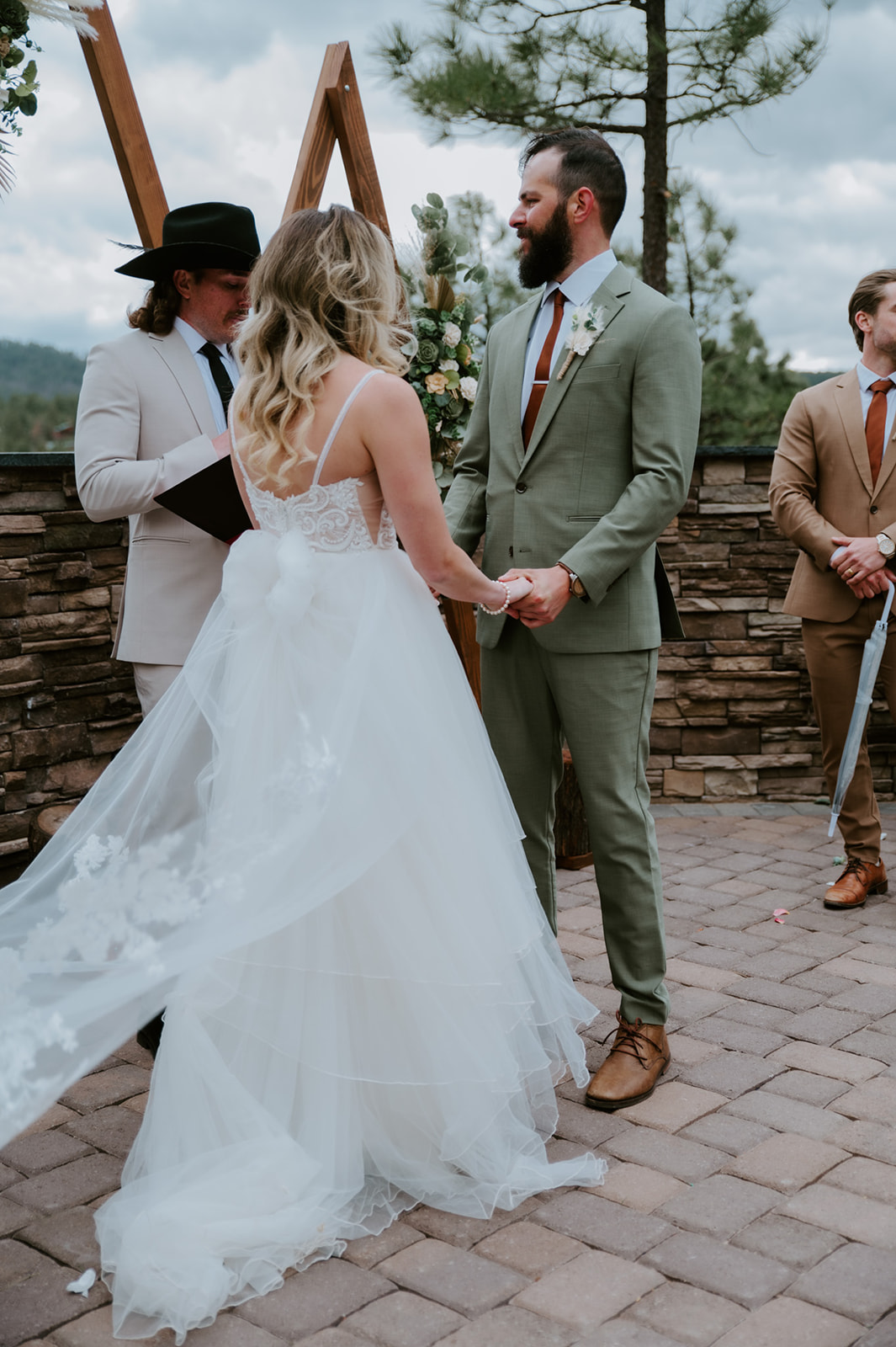 Couple holds hands while exchanging vows beneath wooden triangle arches with mountain views.
