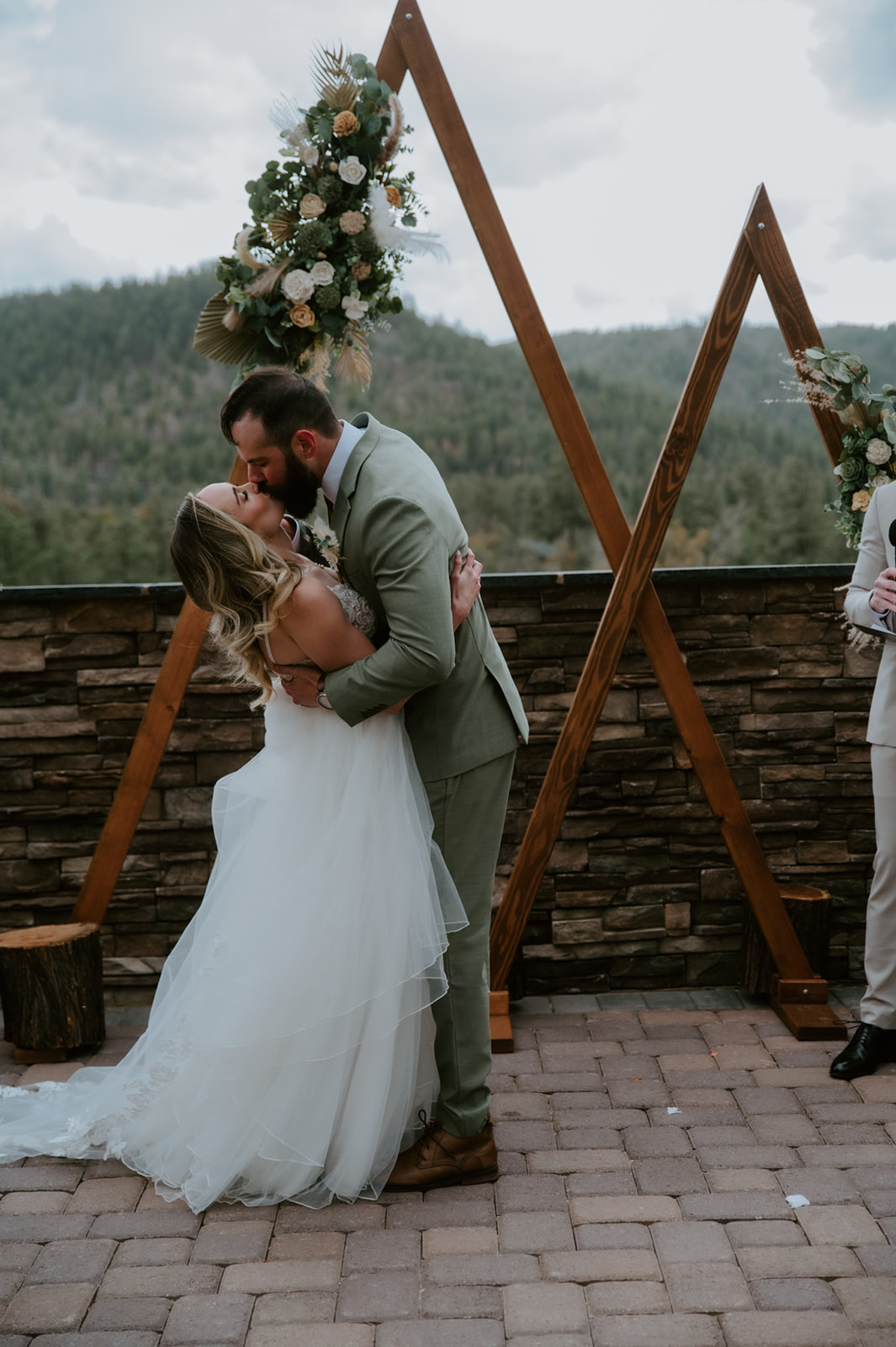 Bride and groom share their first kiss beneath wooden triangle arches after exchanging vows.
