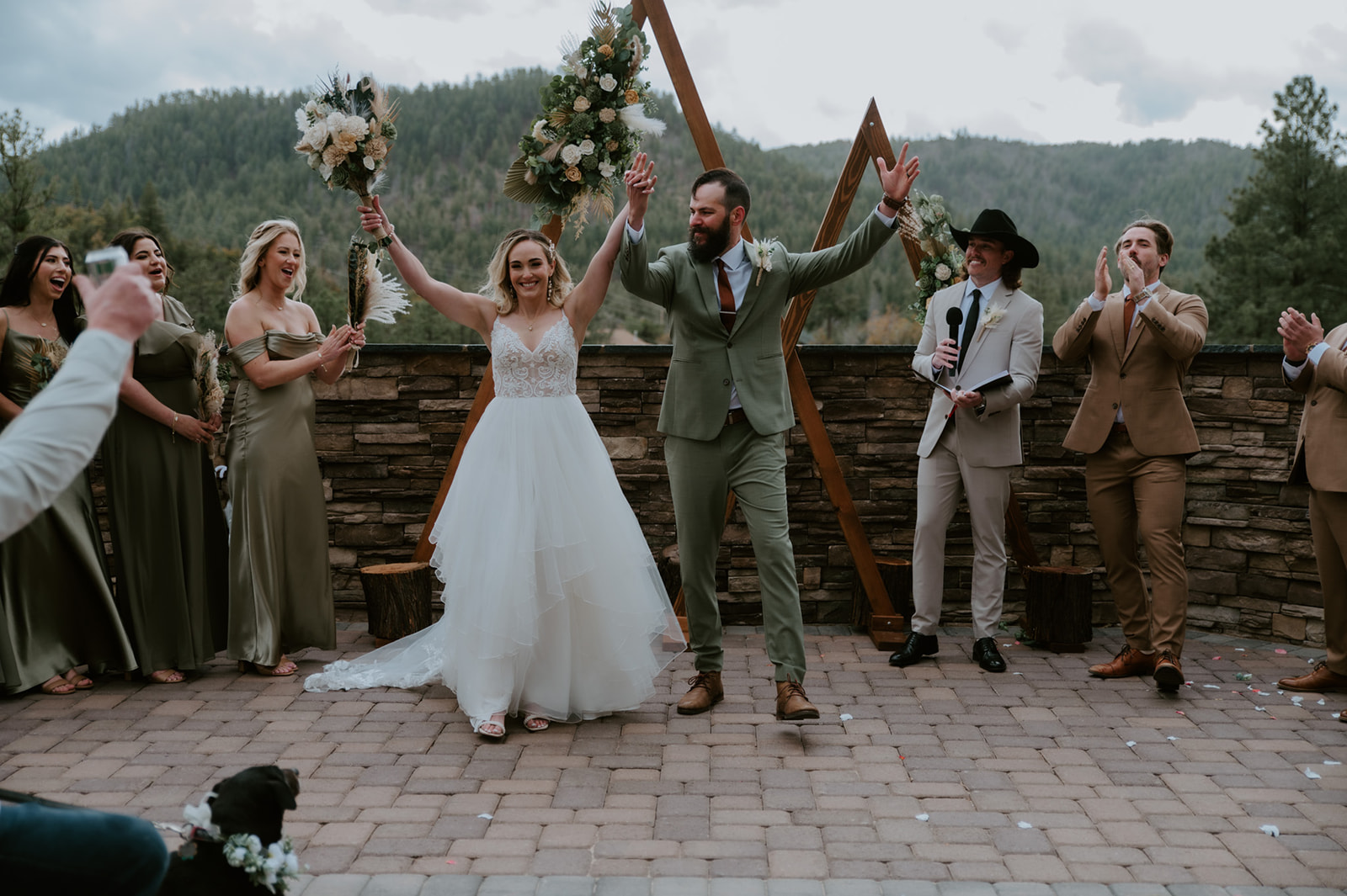Newly married couple celebrates their ceremony with raised hands beneath a floral arch at cabins at strawberry hill.
