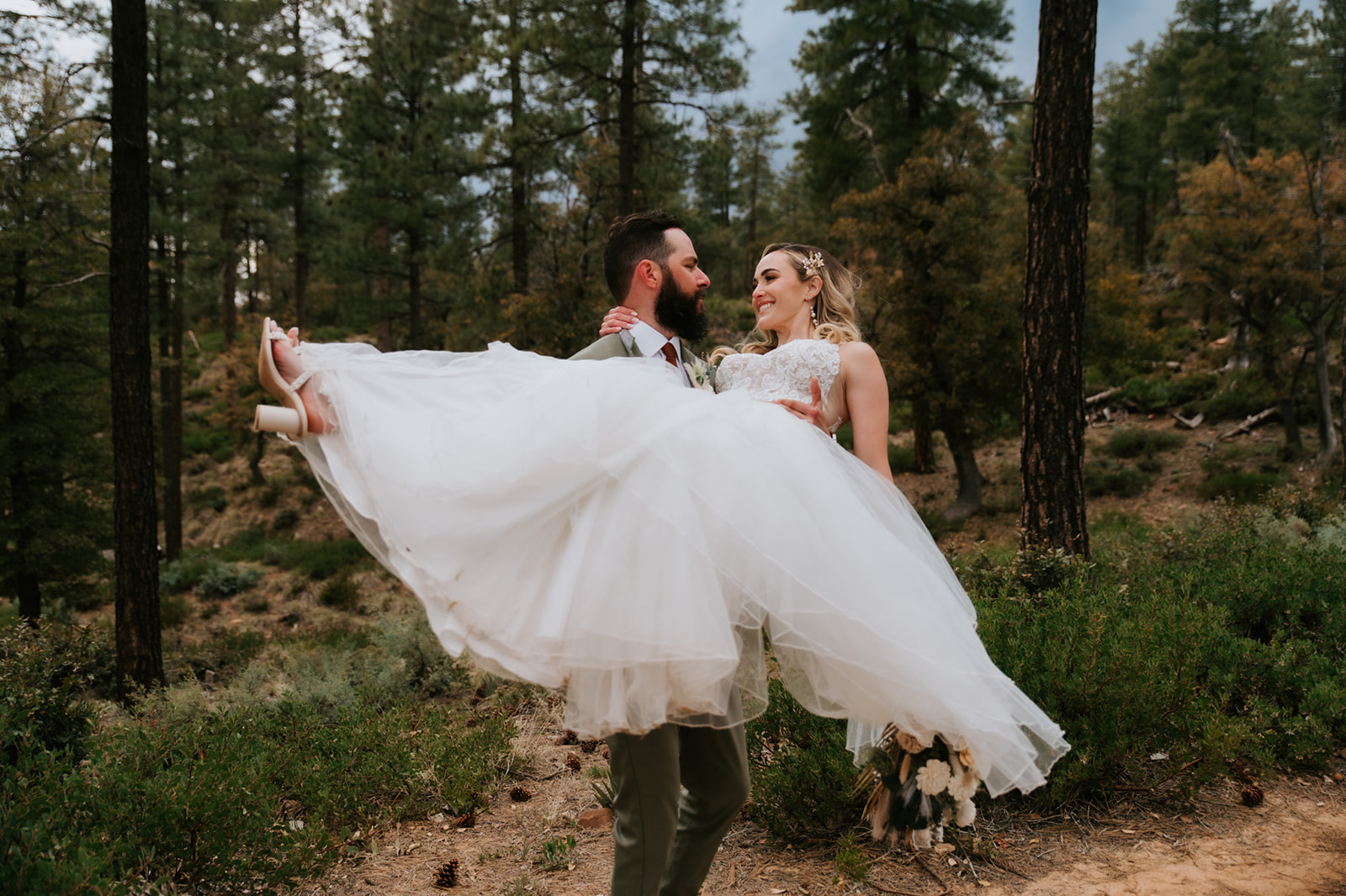 Groom carries his bride through a forest trail for romantic portraits at cabins at strawberry hill.
