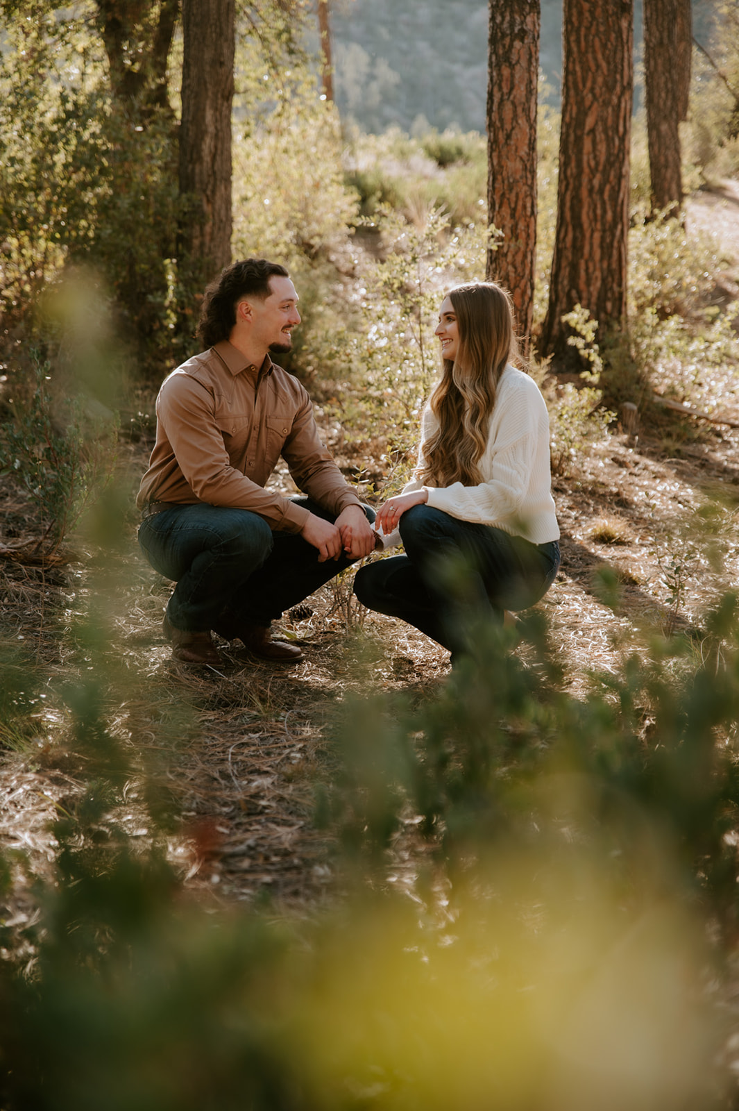 Engaged couple sitting together in the forest, sharing conversation and smiles among the pines.