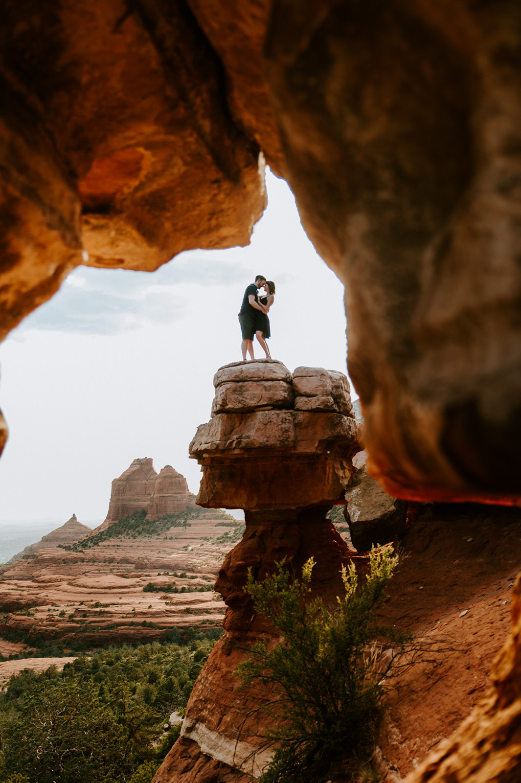 Wide landscape photo of a couple embracing atop Merry Go Round Rock Sedona, framed by dramatic sandstone cliffs.