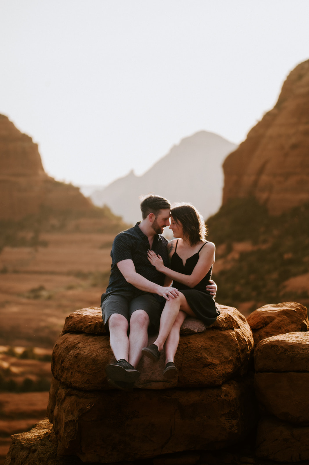 Couple cuddling together on a sandstone ledge during their Merry Go Round Rock Sedona engagement session.