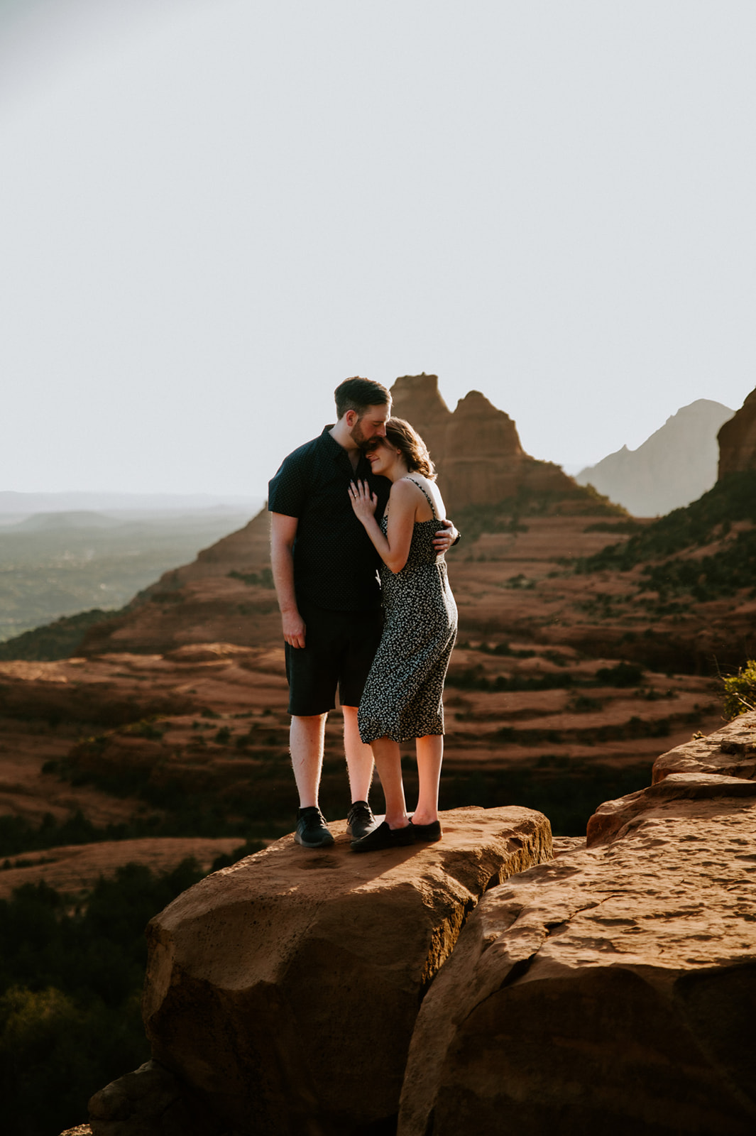 Quiet embrace on a sandstone overlook with golden light illuminating Sedona's iconic red rock landscape.