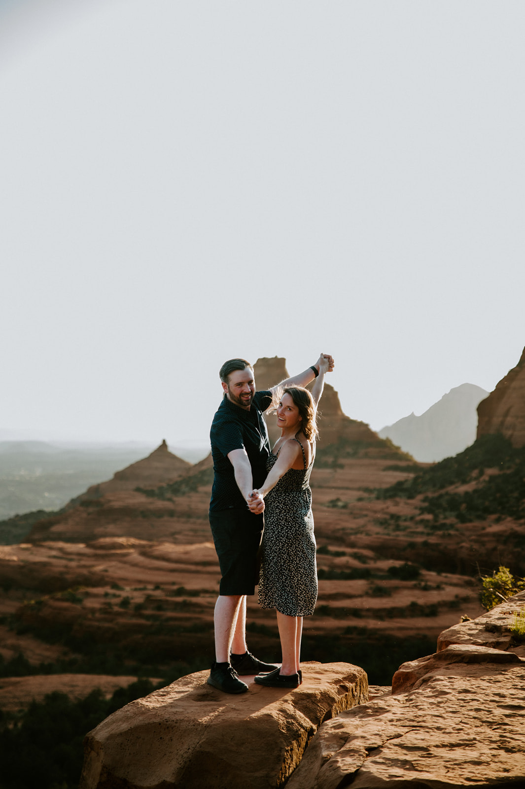Couple holding hands and laughing on a sandstone overlook during their Merry Go Round Rock Sedona engagement session.