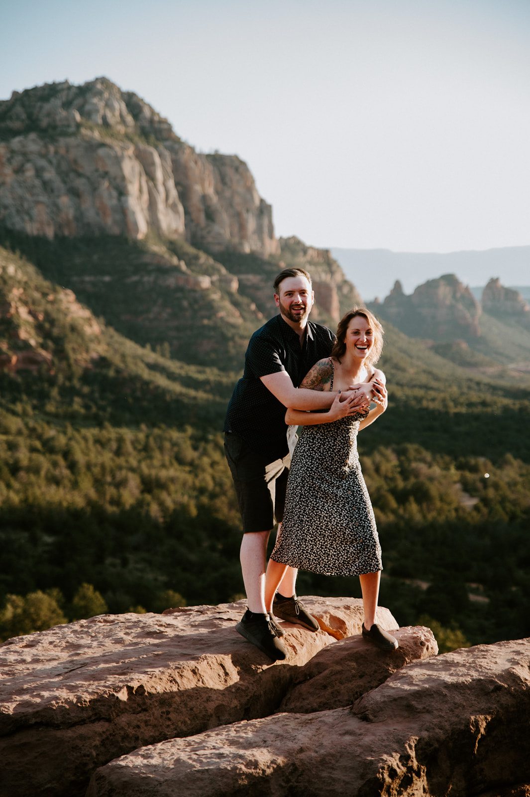 Playful couple laughing together on a sandstone overlook with panoramic views of Sedona's red rock landscape.