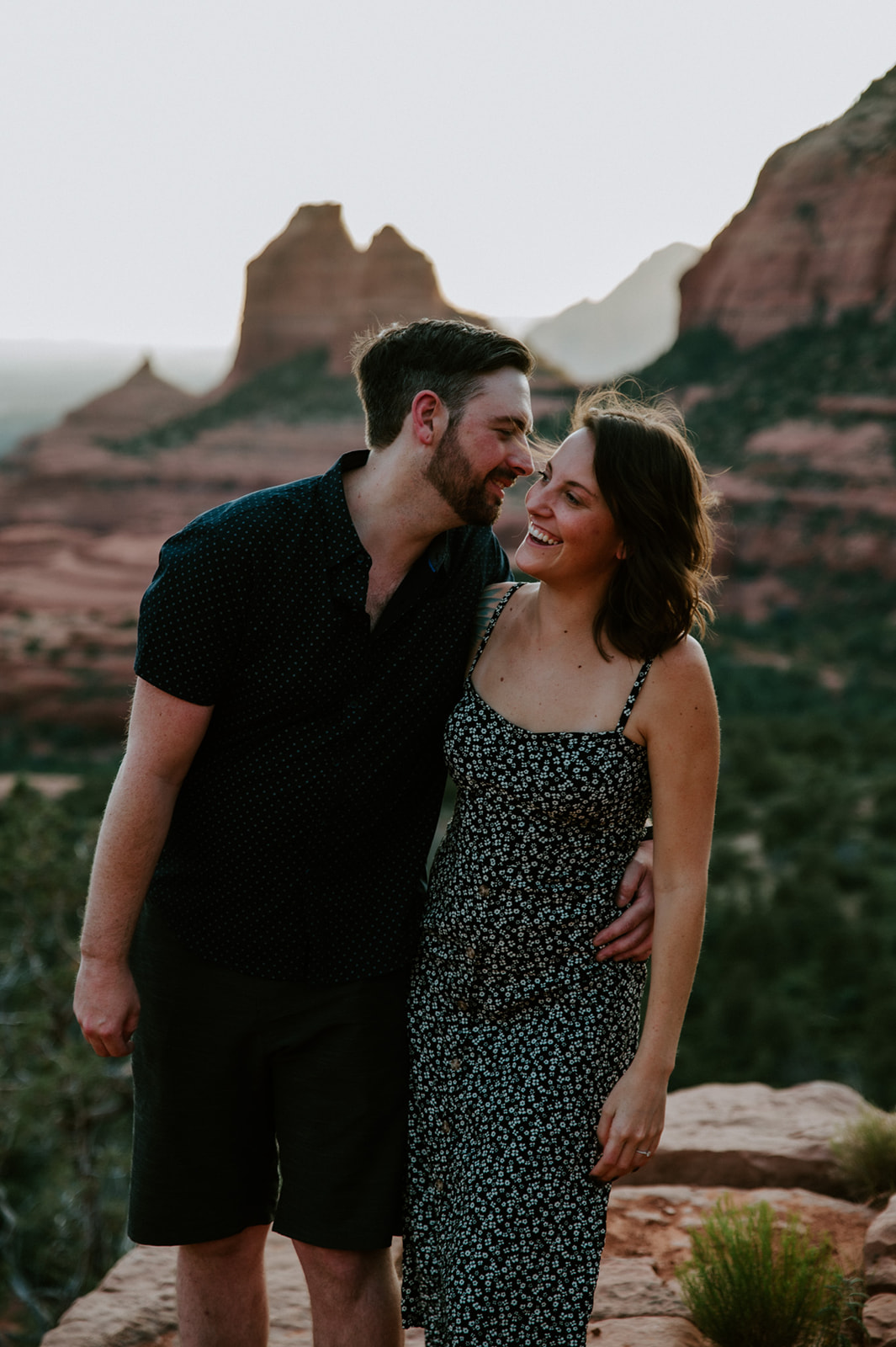 Couple smiling together with Bell Rock in the distance during their Merry Go Round Rock Sedona engagement photos.