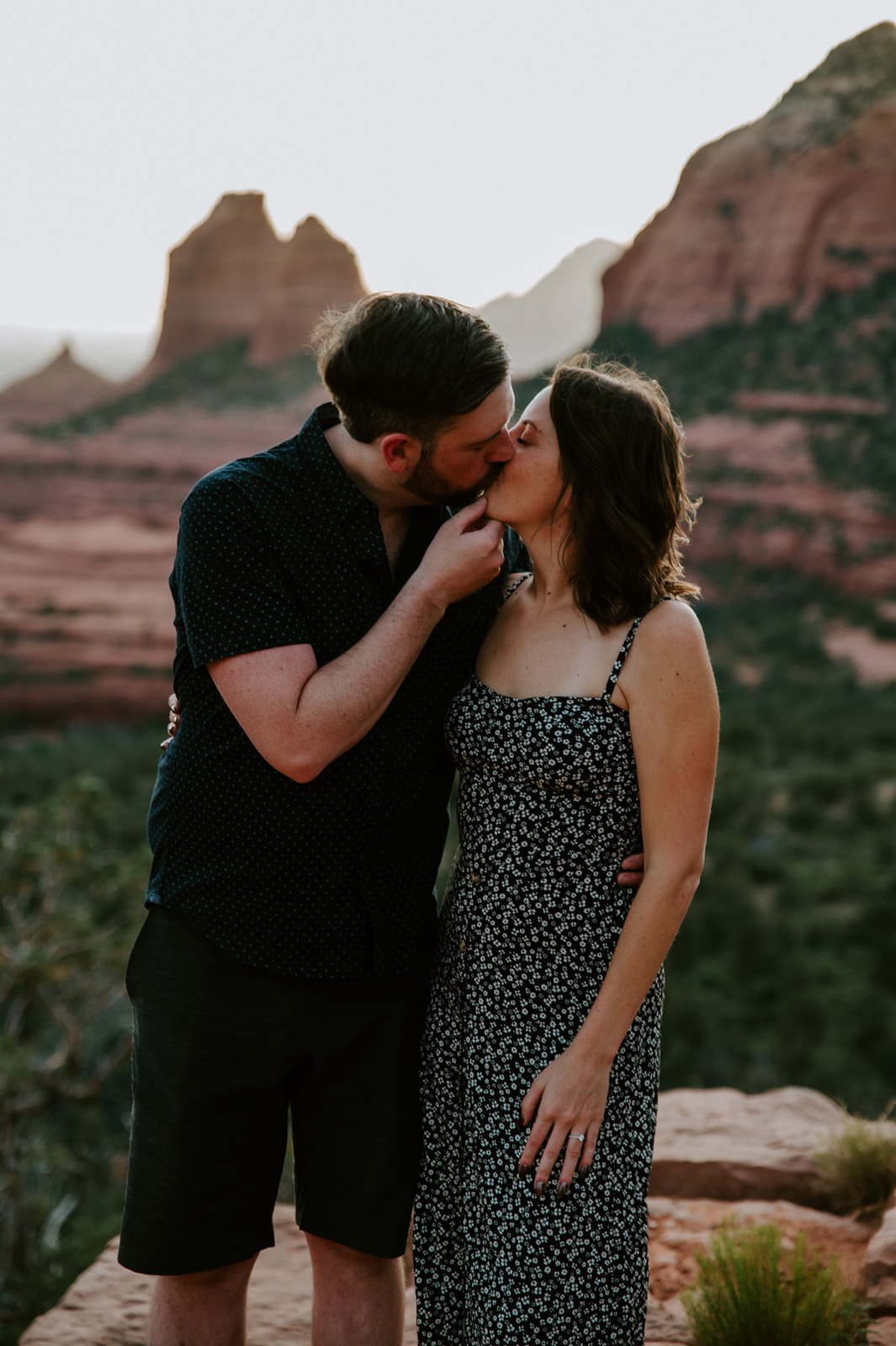 Romantic kiss during Arizona engagement photos with Sedona's iconic red rock formations in the background.