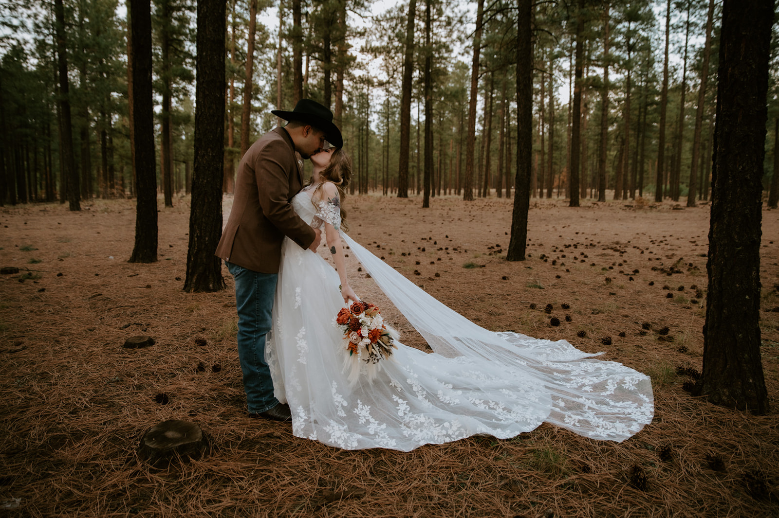 Bride and groom sharing a romantic kiss beneath towering pine trees at The Gathering Place during their fall wedding in Pinetop, Arizona.