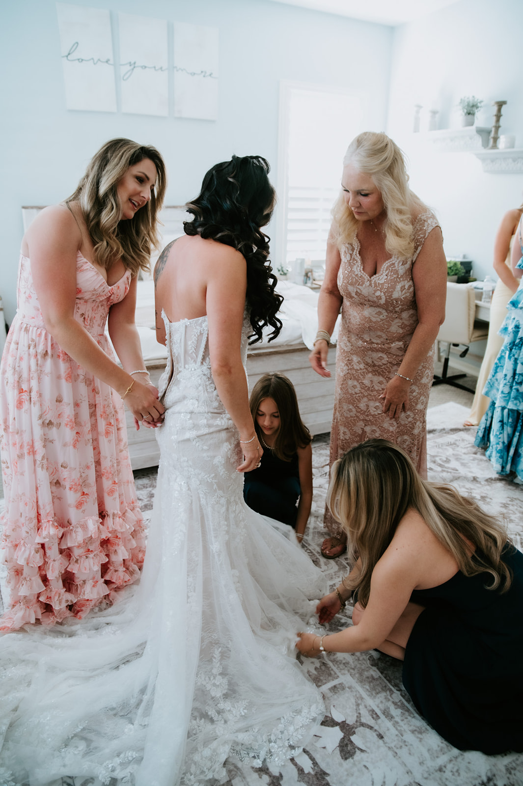 Family and friends help the bride adjust the train of her lace wedding gown before the ceremony.
