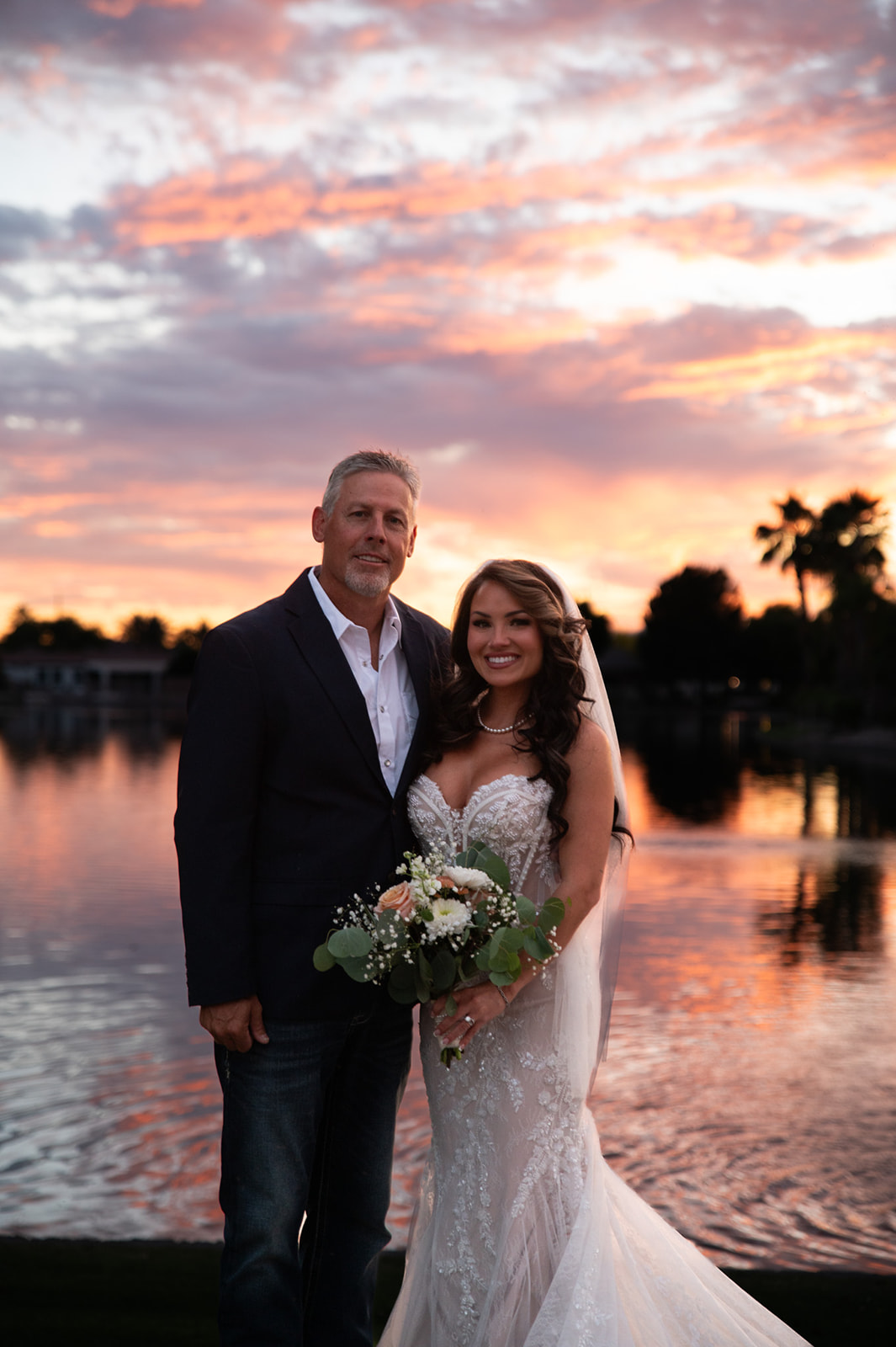 Bride and groom pose beside the water at sunset, capturing romantic backyard wedding ideas with a colorful sky.
