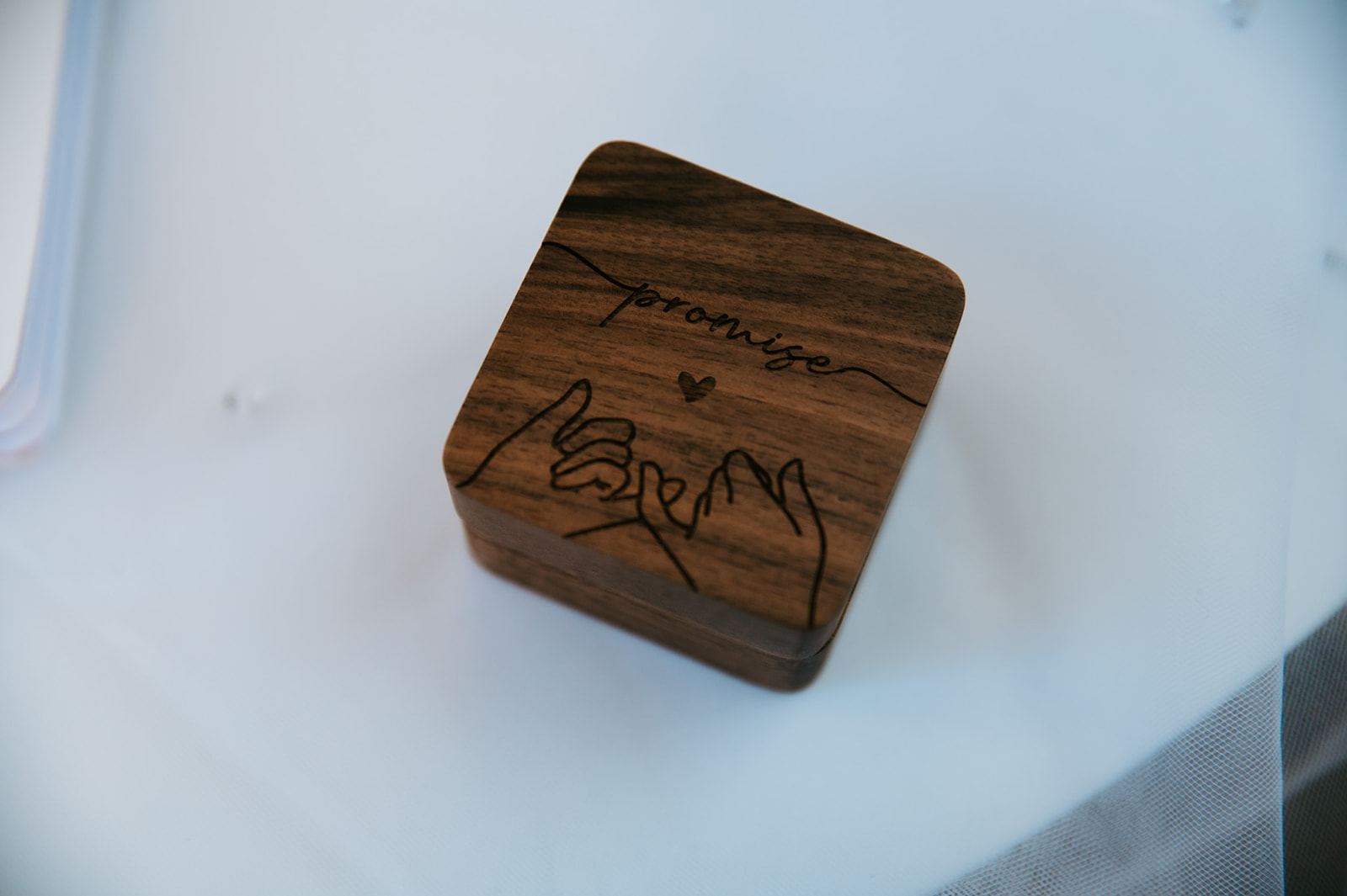 Close-up of a personalized wooden wedding ring box engraved with “Promise” and a hand-holding design.
