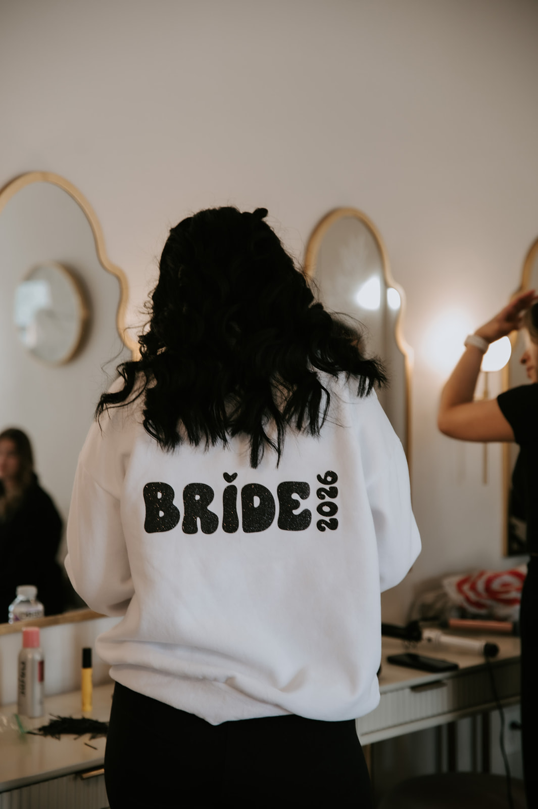 Bride getting ready in a white “Bride 2026” sweatshirt before the wedding ceremony.
