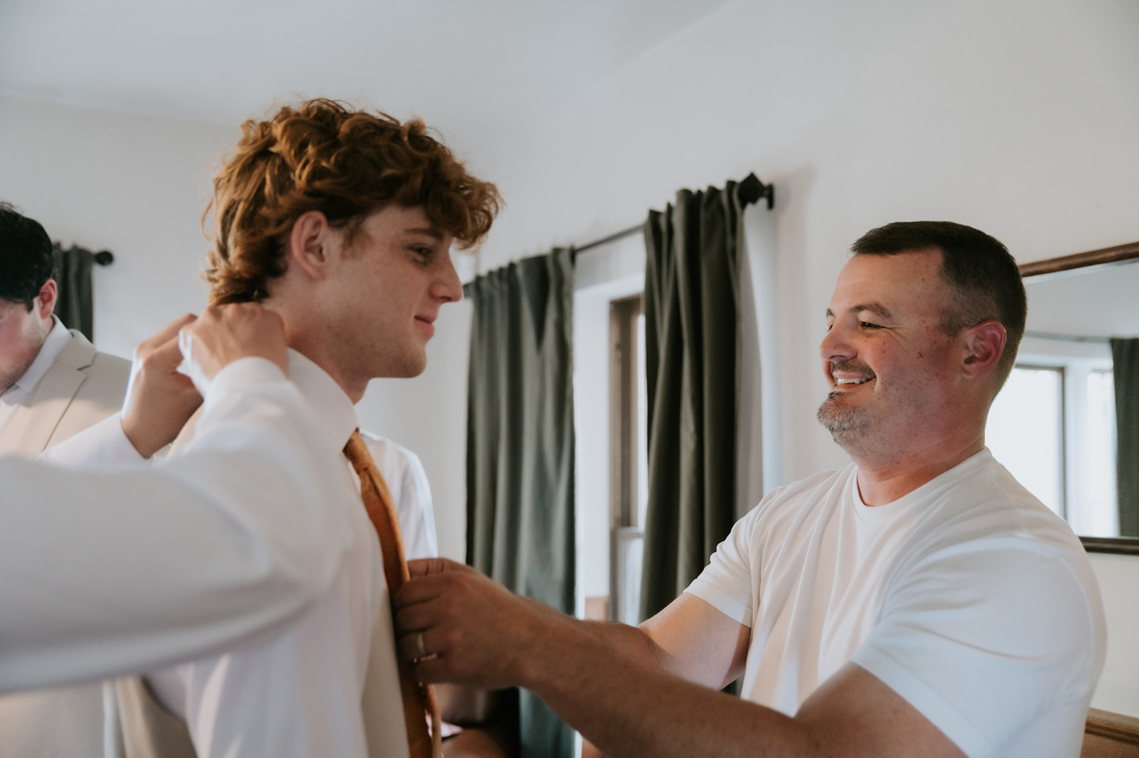 Groomsmen gets help adjusting his tie while getting ready for the wedding.
