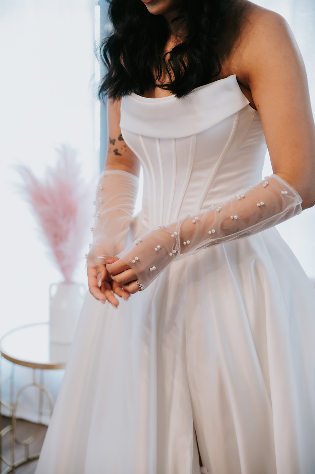 Close-up of the bride’s satin corset wedding dress and sheer pearl-embellished gloves.
