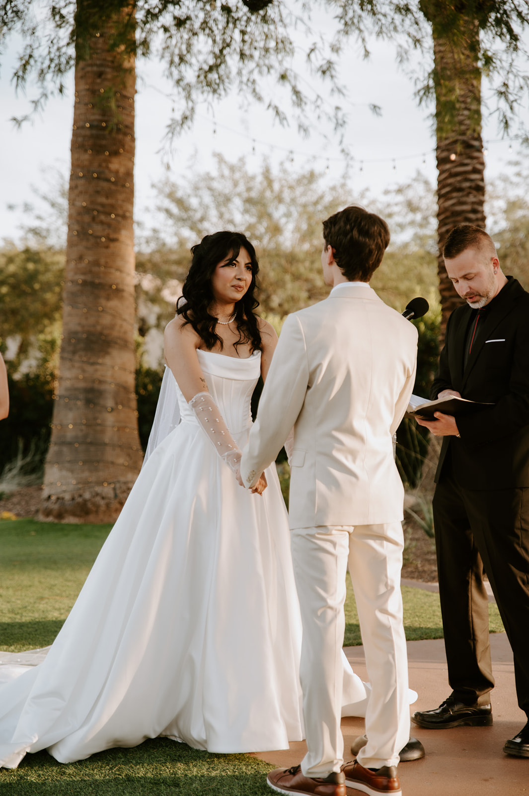 Bride and groom hold hands while exchanging vows during a golden-hour garden ceremony.
