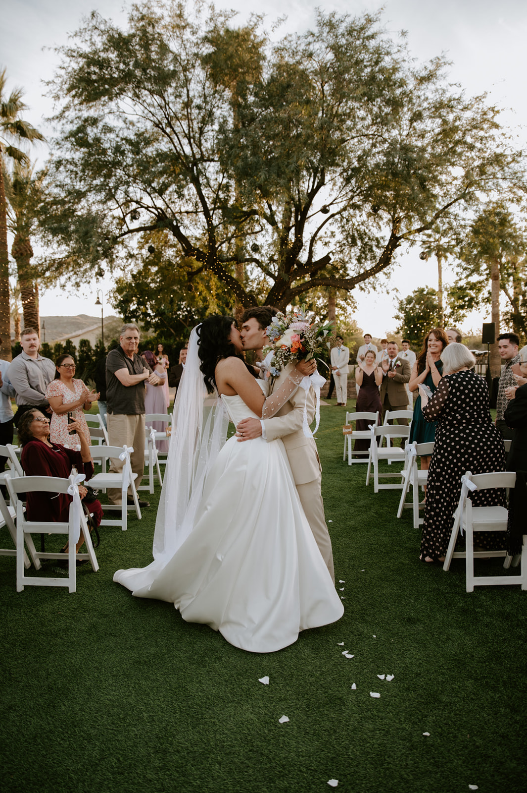 Bride and groom kiss in the aisle as guests celebrate around them at Secret Garden by Wedgewood Weddings.
