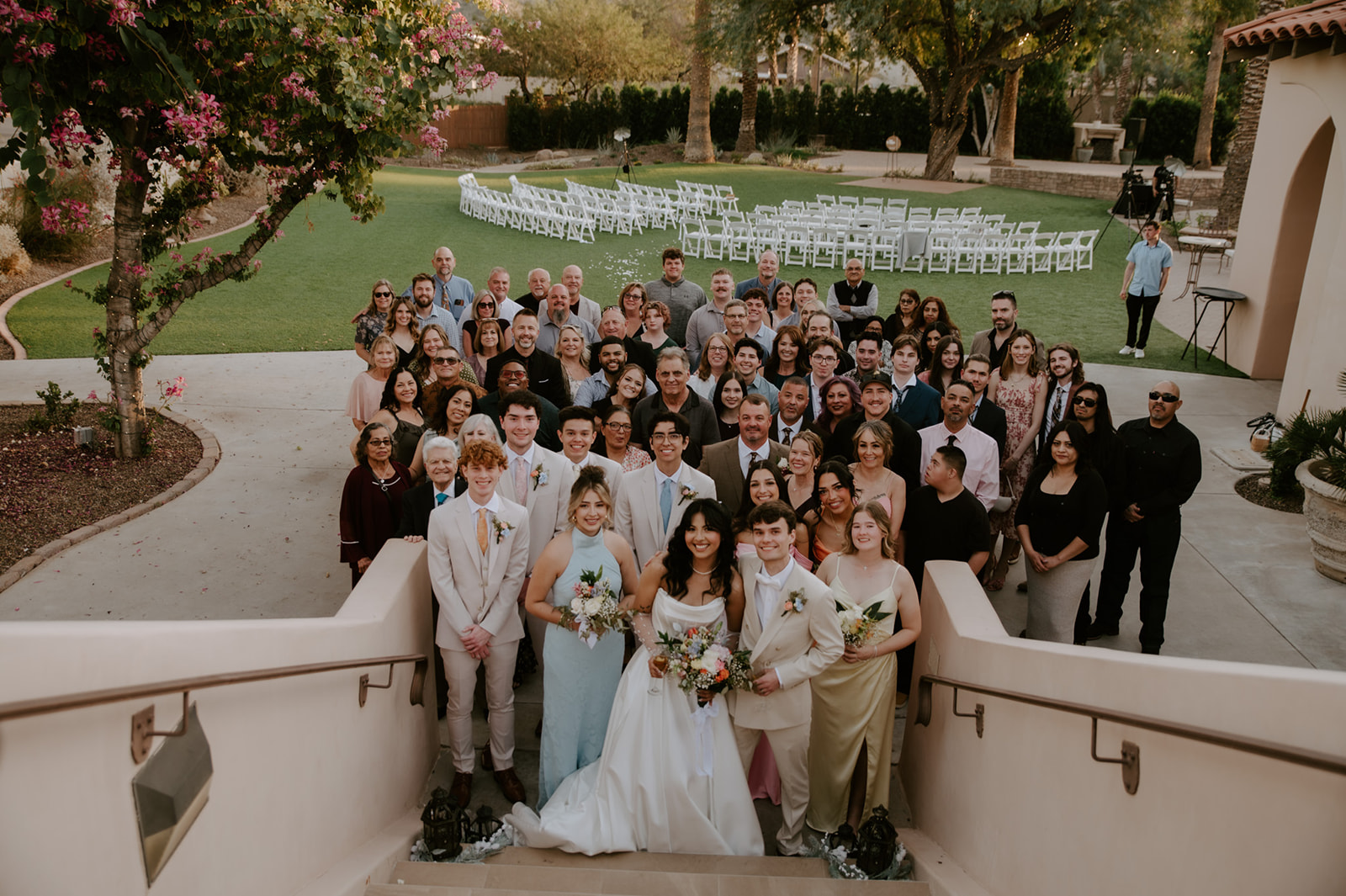 Newlyweds gather with their wedding party and guests for a large group photo overlooking the ceremony lawn.
