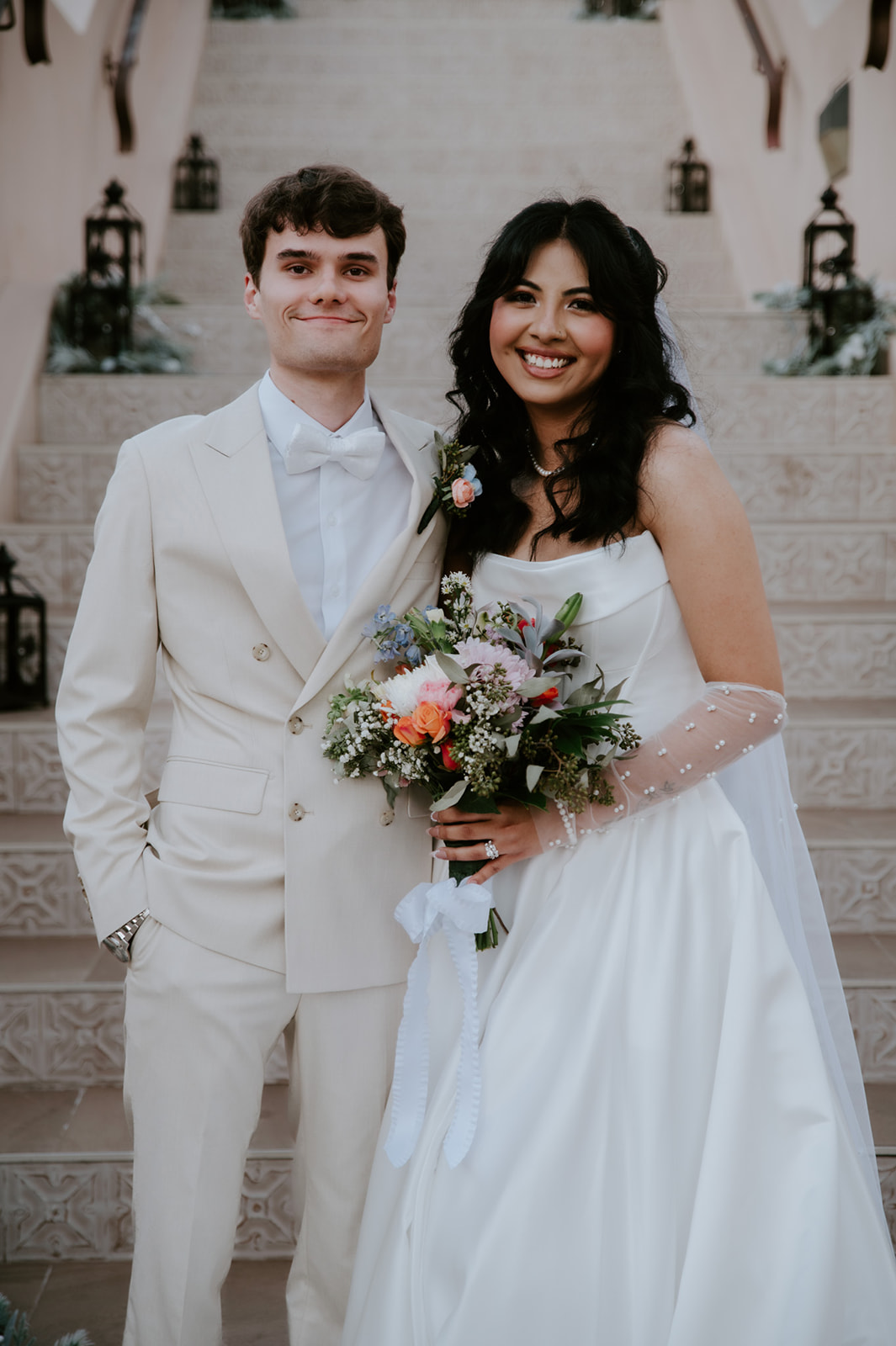 Bride and groom smile for a formal wedding portrait on tiled steps.
