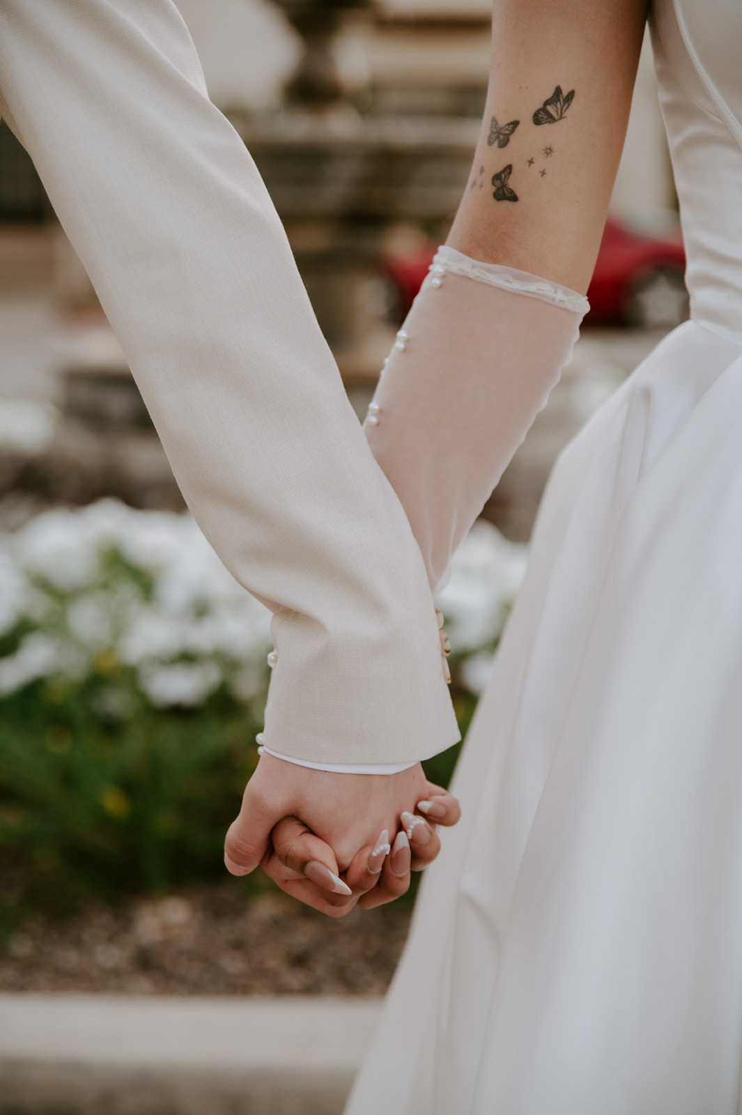 Close-up of the bride and groom holding hands, highlighting the bride’s pearl glove and butterfly tattoos.
