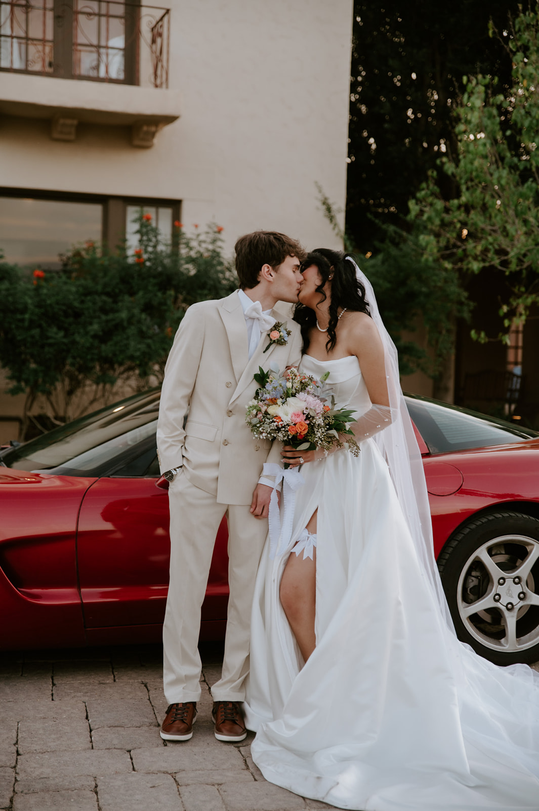 Newlyweds kiss beside a red sports car outside Secret Garden by Wedgewood Weddings.
