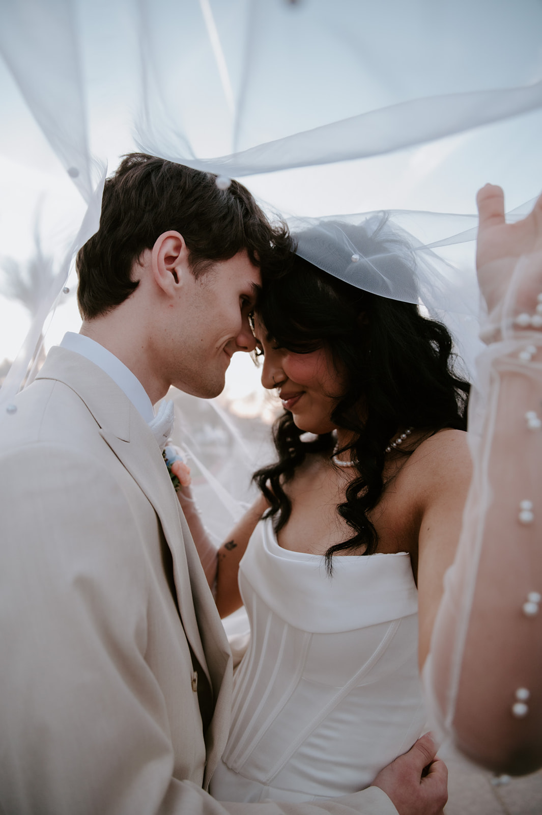 Bride and groom share an intimate moment beneath her softly draped wedding veil.
