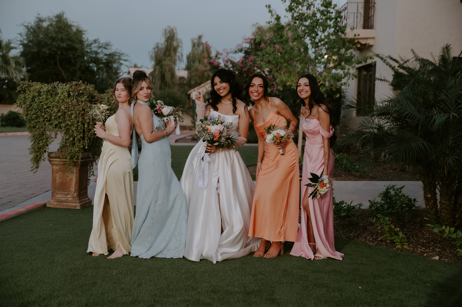 Bride poses with bridesmaids in colorful pastel dresses and floral bouquets at Secret Garden by Wedgewood Weddings.
