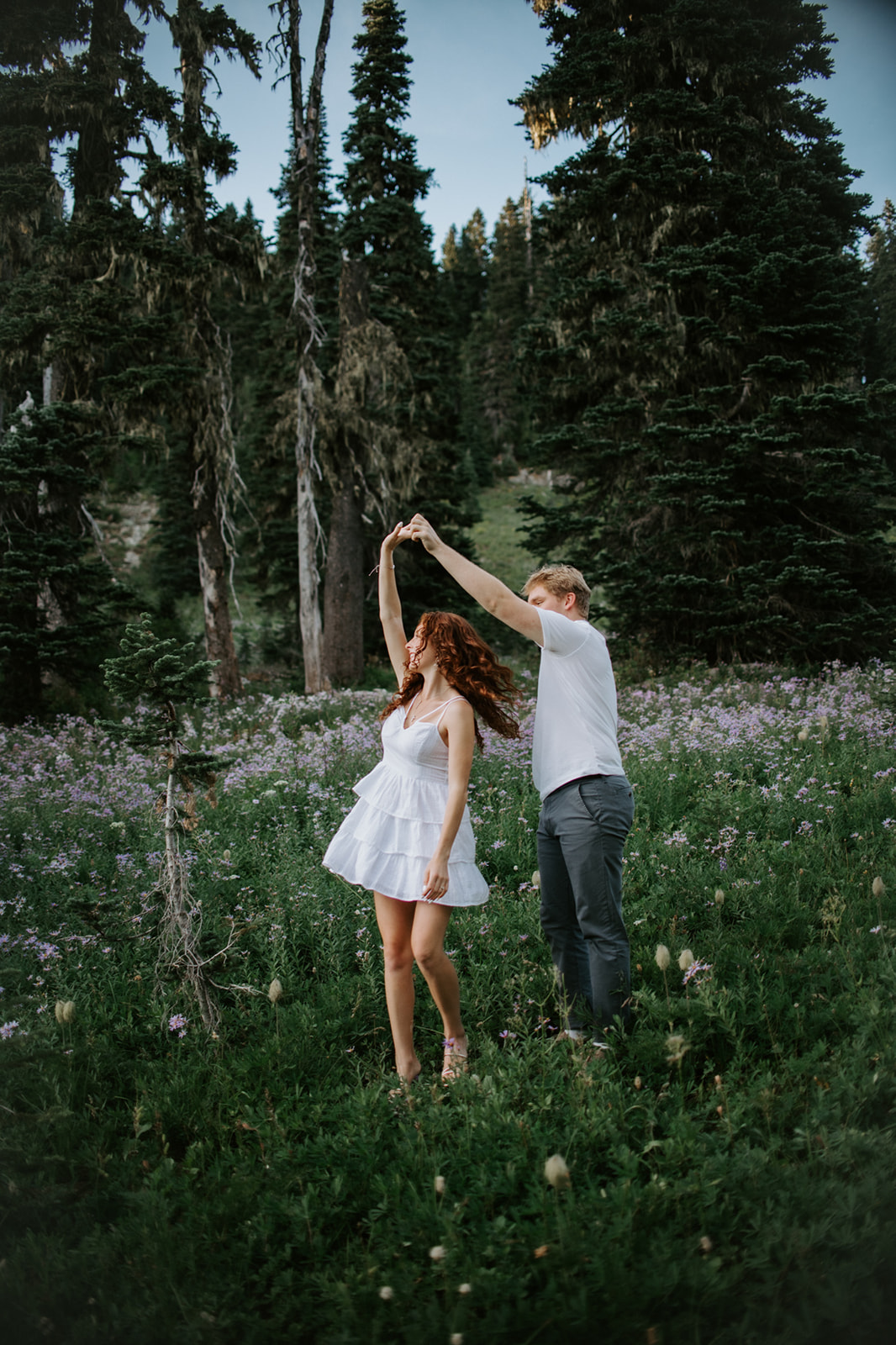 Couple dancing together in a colorful alpine wildflower meadow surrounded by dense evergreen forest.