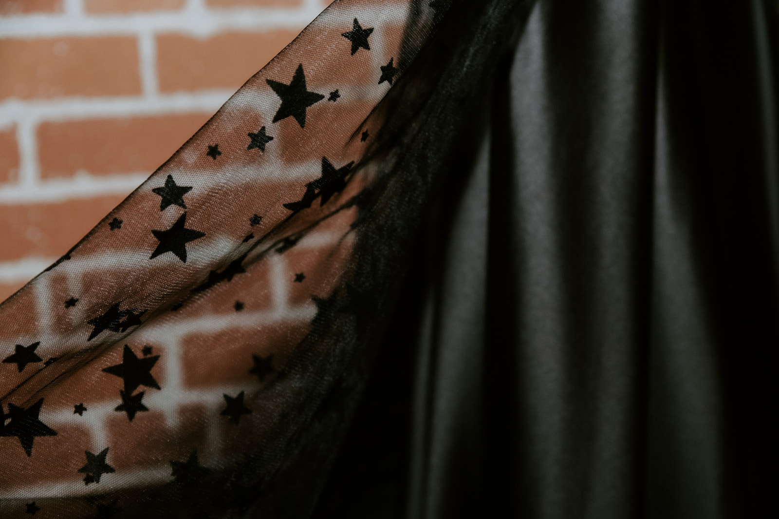 Close-up of sheer black wedding dress fabric covered in embroidered stars against a brick wall.