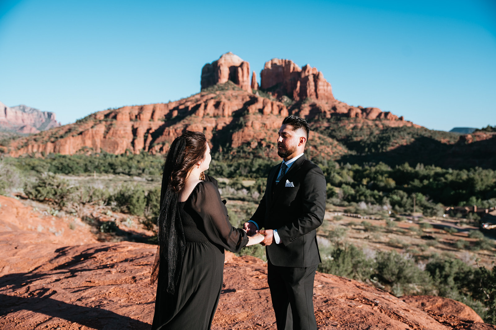 Couple holding hands on red rocks during their non traditional wedding with Arizona's red mountains in the background.