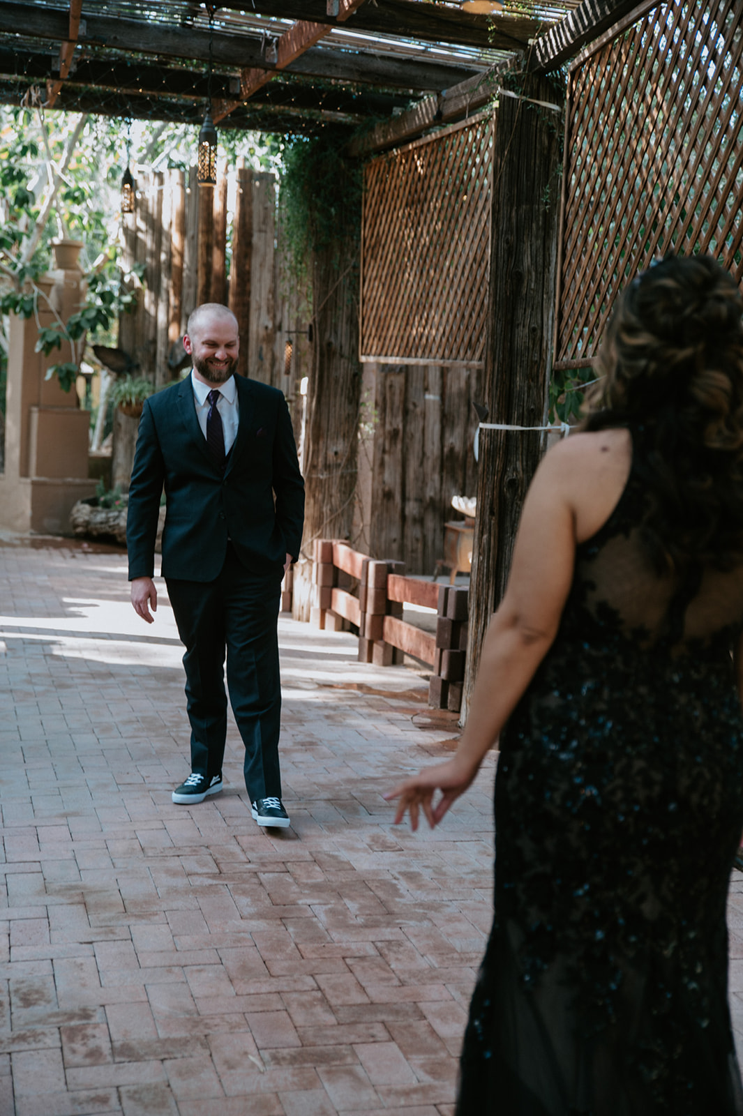 Partner smiling as he walks toward the bride in a black sequin wedding dress during their garden first look.