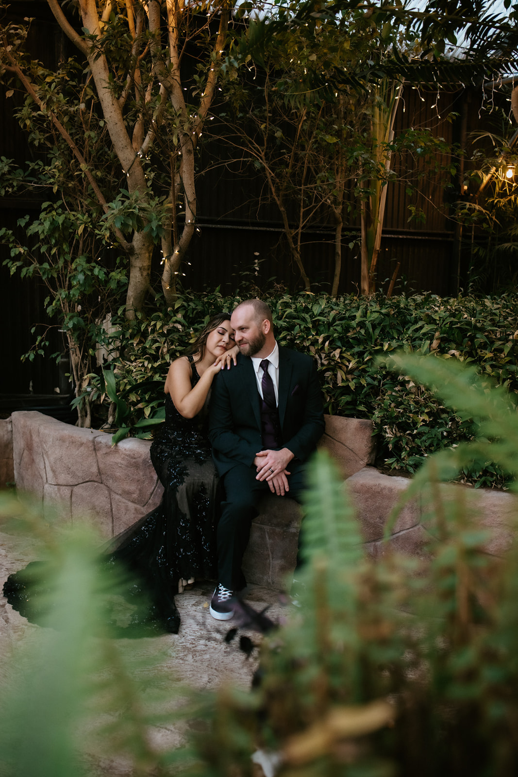 Couple cuddling together beneath string lights after their non traditional wedding in a lush garden setting.