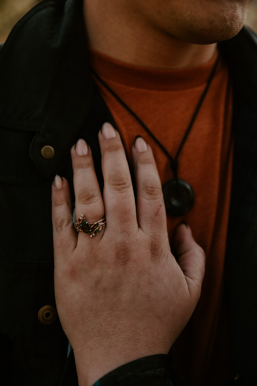 Close-up of a unique engagement ring against layered earth-tone clothing, offering detail inspiration for what to wear for engagement photos.