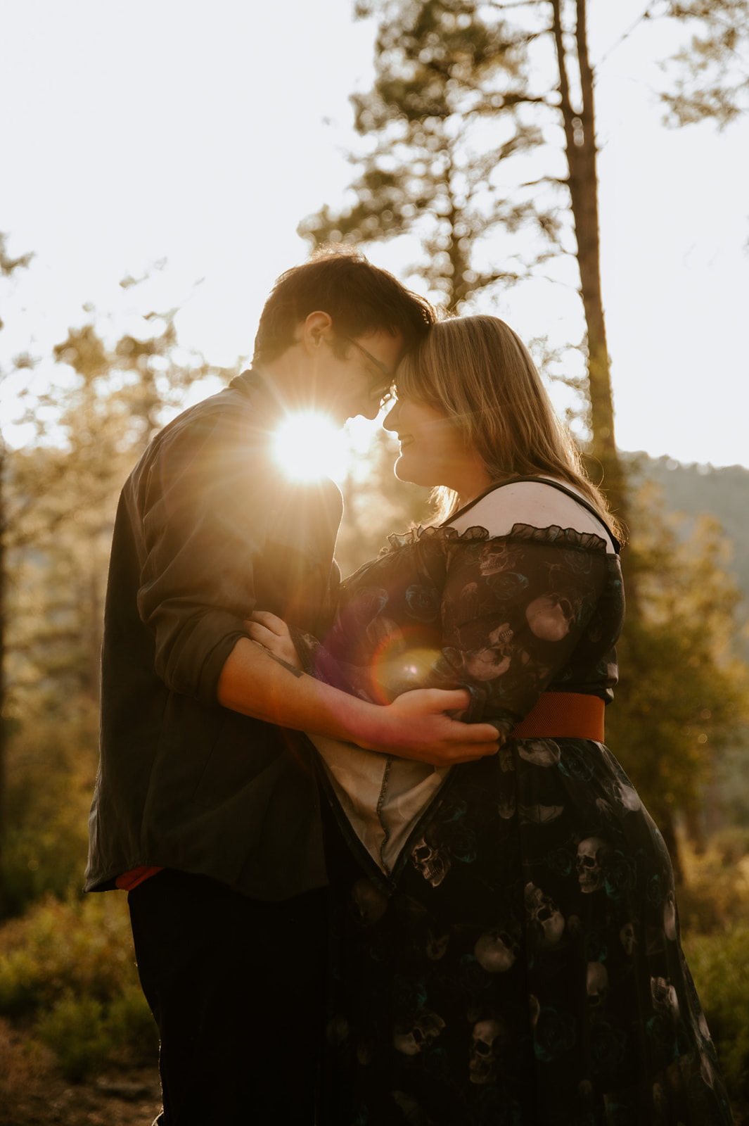 Couple standing forehead to forehead in warm golden sunlight during their romantic forest engagement session.