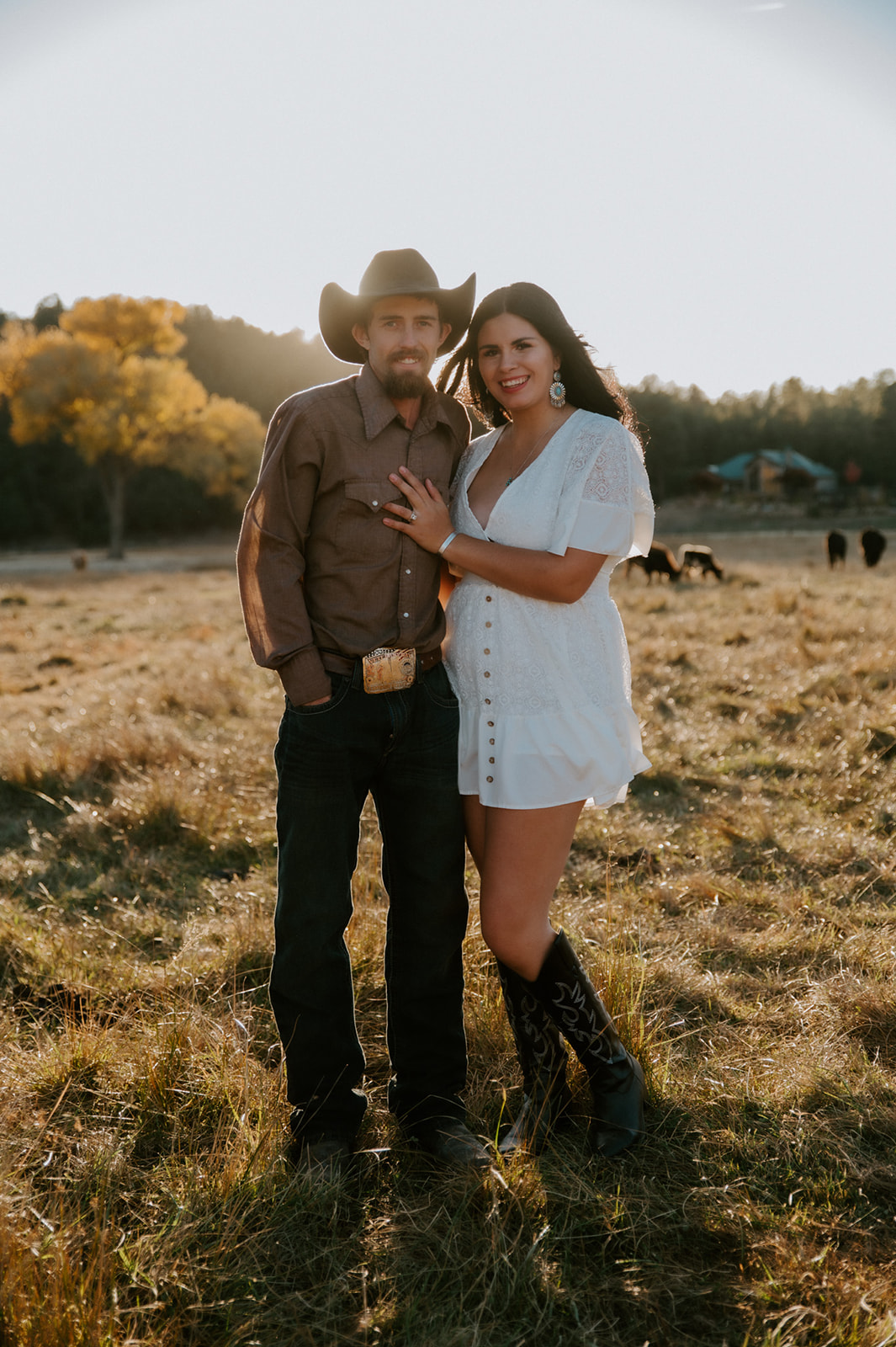 Couple embracing in a golden field, with a white lace dress, cowboy boots, and earth tones creating a romantic Western look.