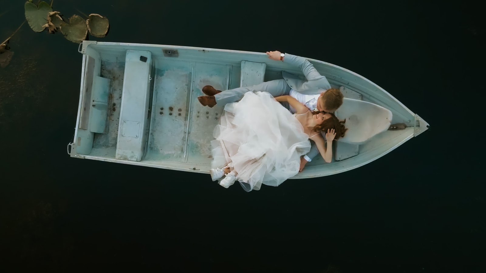 Aerial view of newlyweds lying together in a rowboat surrounded by dark water after their wedding in seattle.