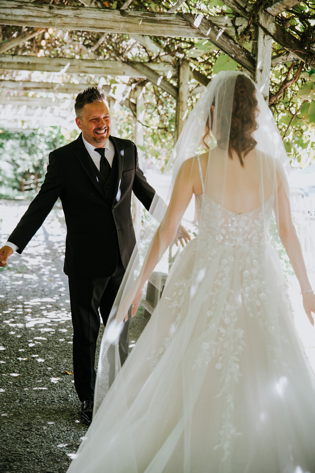 Bride and a man in a black suit sharing a joyful first look beneath a wooden pergola during a wedding in seattle.