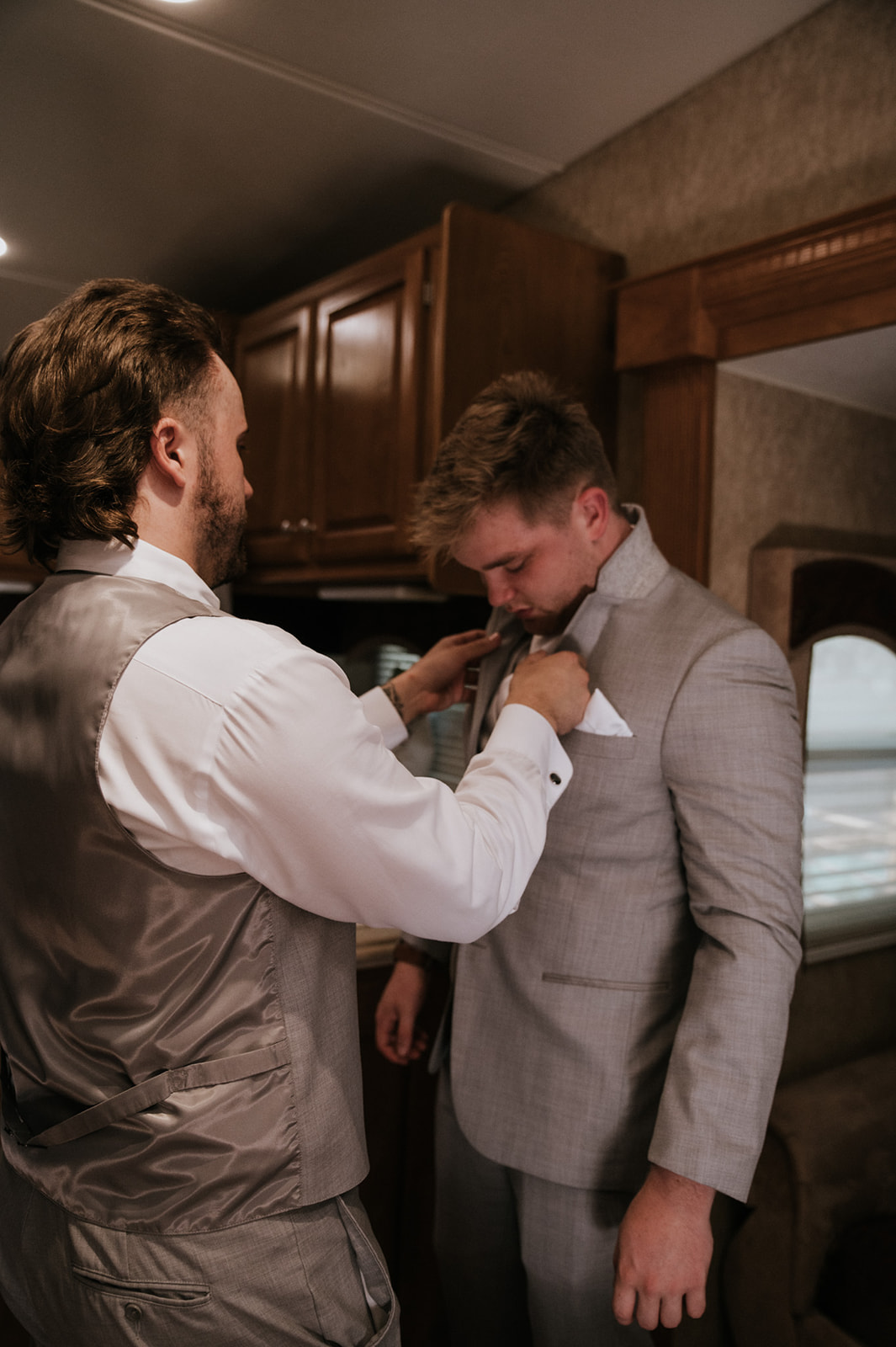 Groomsman adjusting the groom's light gray suit jacket while getting ready for his wedding in seattle.