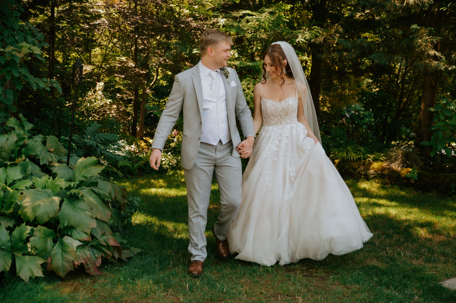 Bride and groom holding hands while walking through a lush green garden after their wedding in seattle.