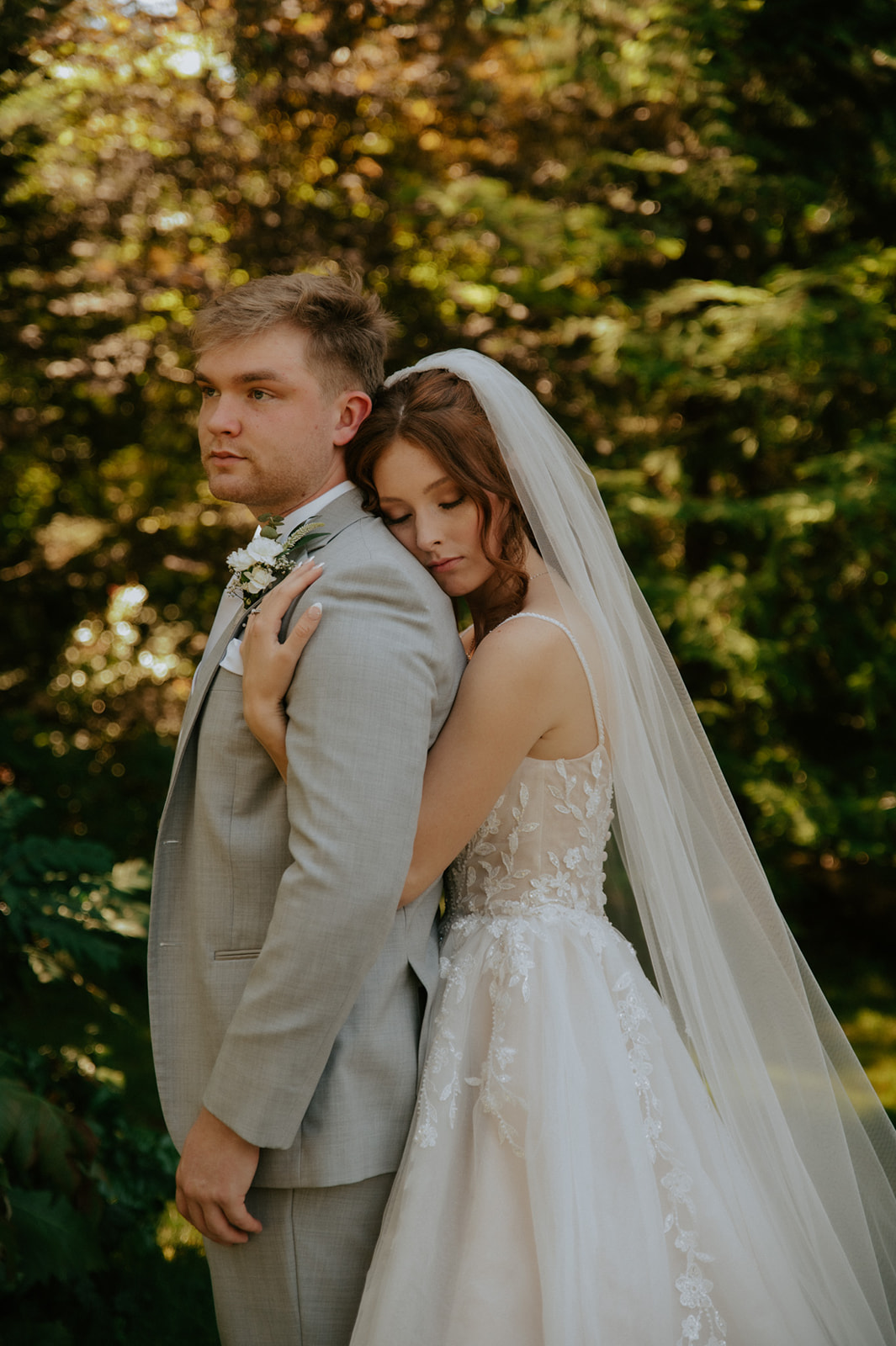 Bride resting her head against the groom's shoulder while embracing him in a sunlit garden.