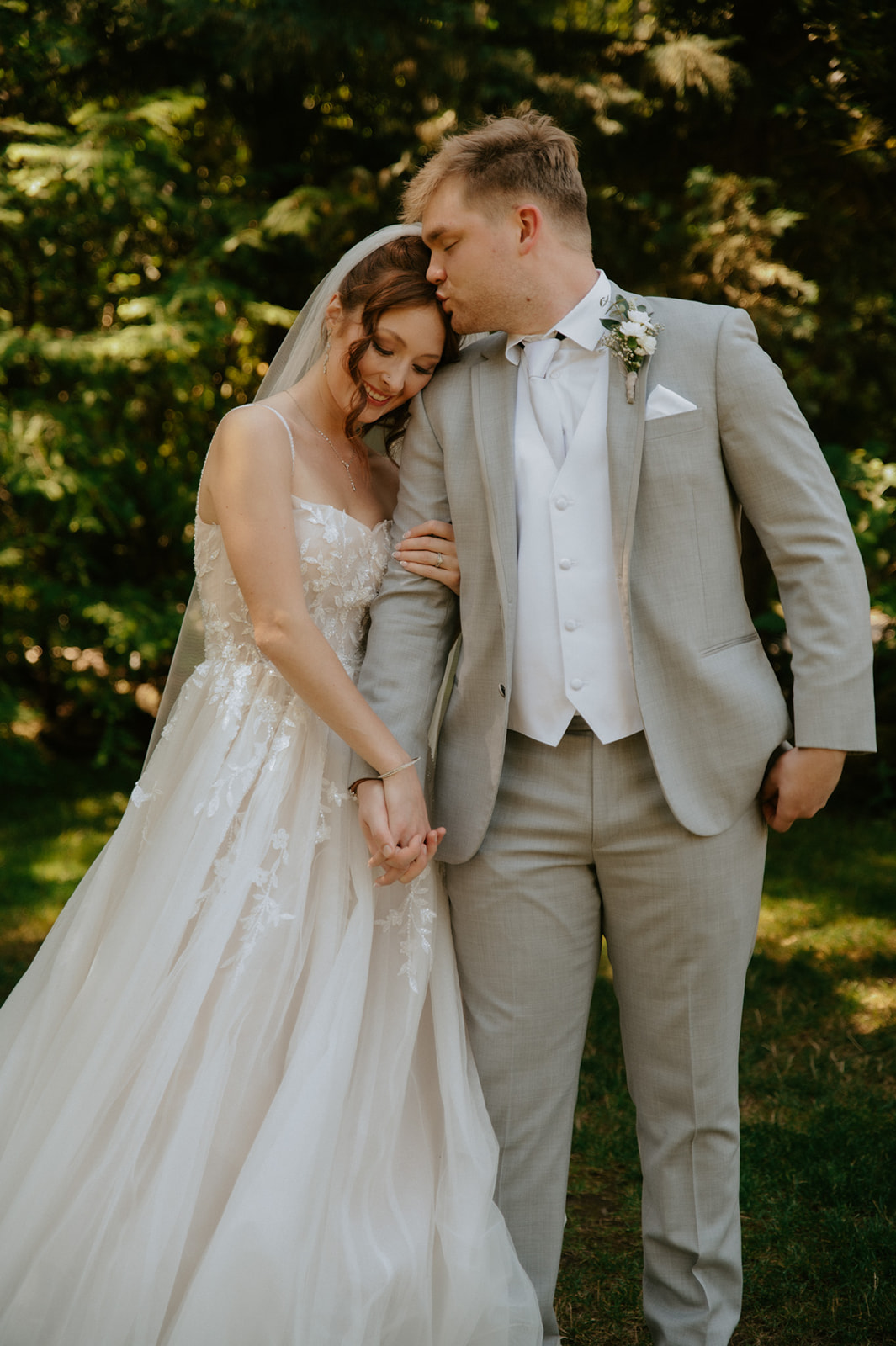 Groom kissing his bride's forehead as they hold hands during their outdoor wedding in seattle.