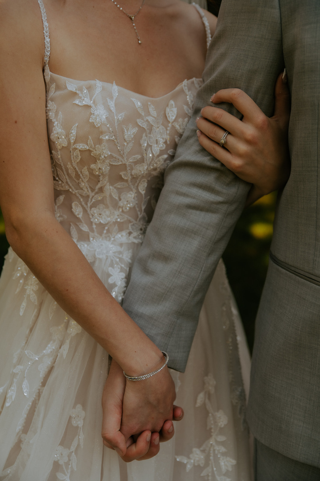 Close-up of newlyweds holding hands, highlighting the bride's floral lace gown and wedding ring during their wedding in seattle.