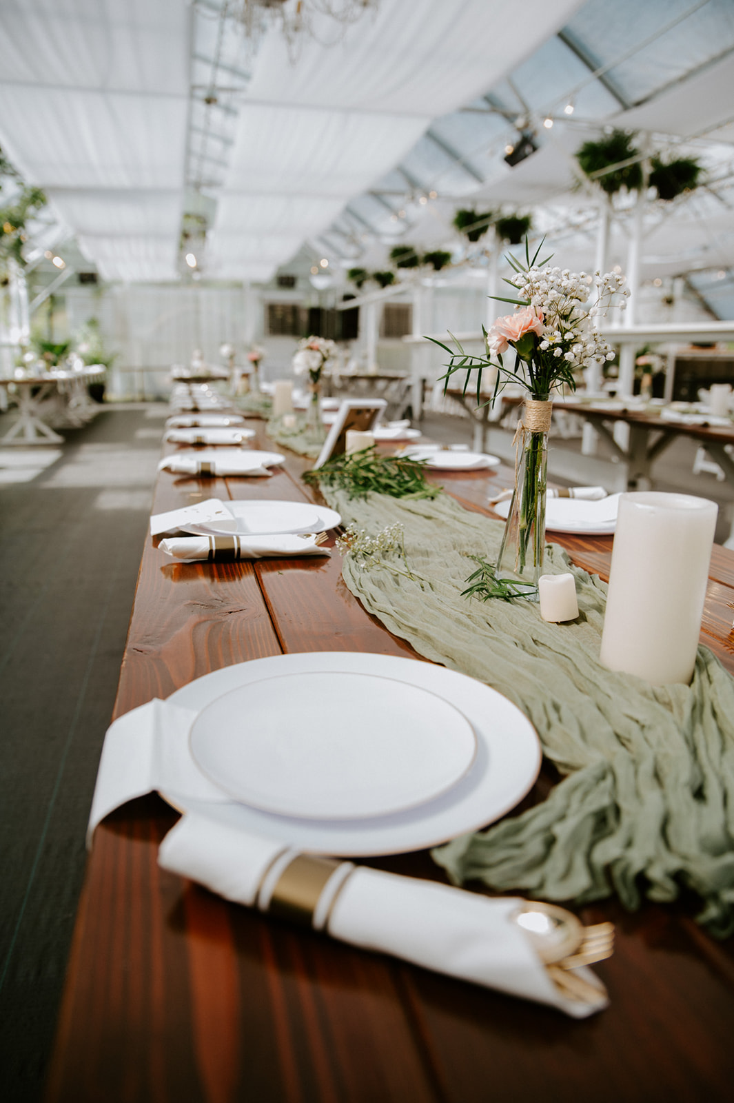 Wedding reception table decorated with white plates, sage green table runners, candles, and delicate floral centerpieces.