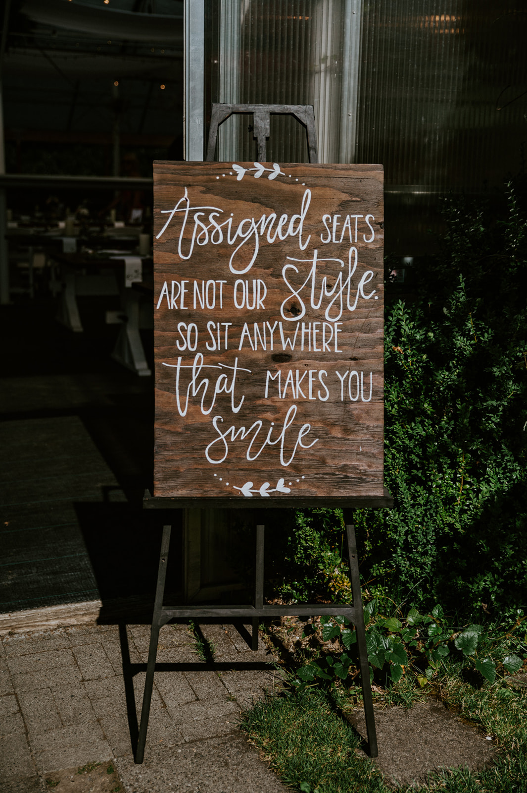 Wooden wedding reception sign reading "Assigned seats are not our style" displayed outside the venue during a wedding in seattle.